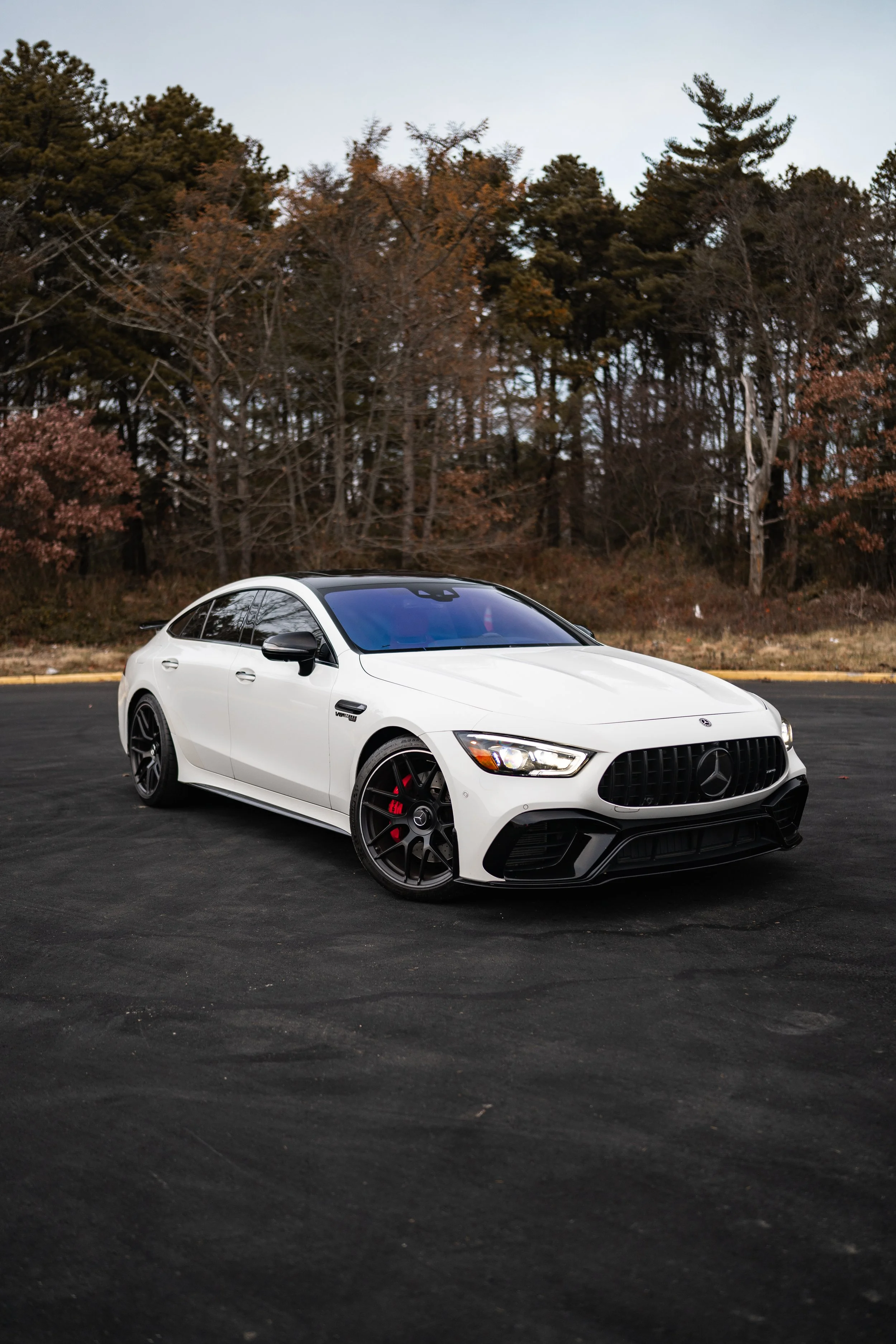 A white Mercedes-Benz sports car parked on asphalt with a background of trees and overcast sky.
