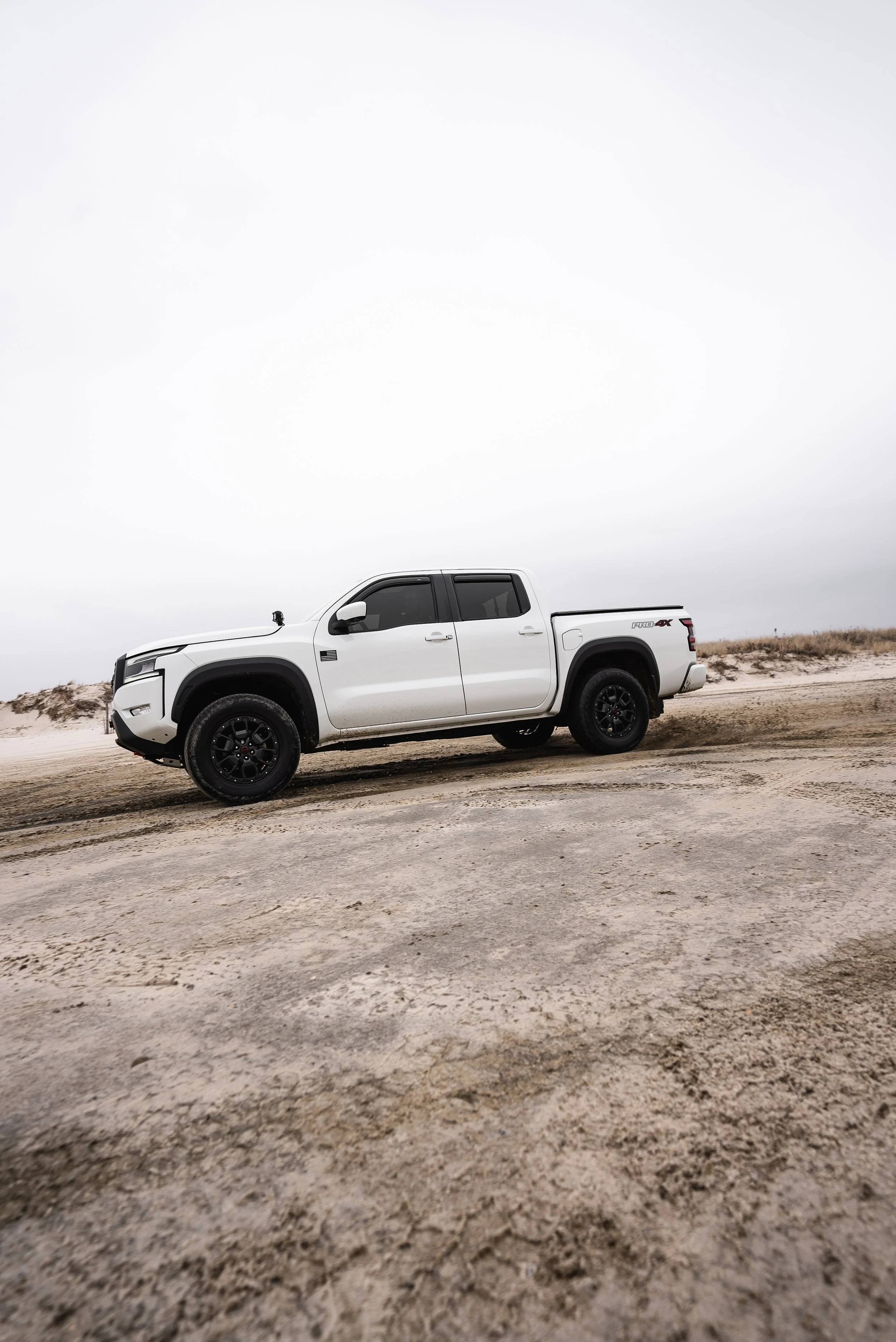 White pickup truck parked on a sandy beach against a cloudy sky.