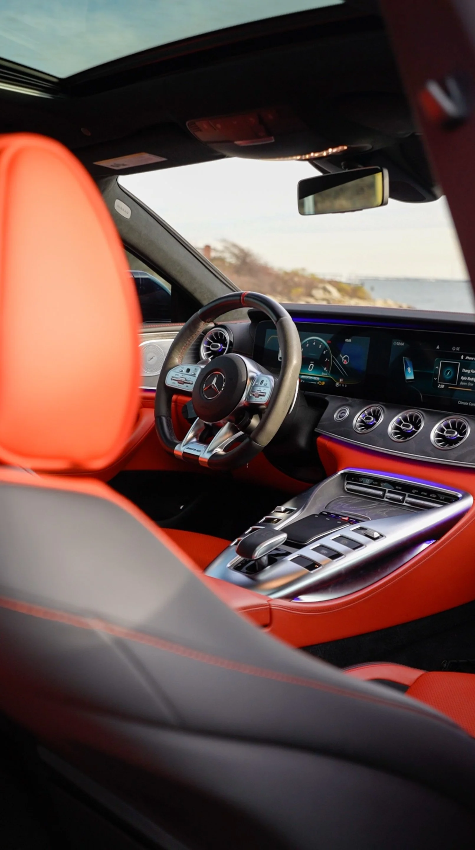Interior of a luxury car with a digital dashboard, Mercedes-Benz steering wheel, and red leather seats.