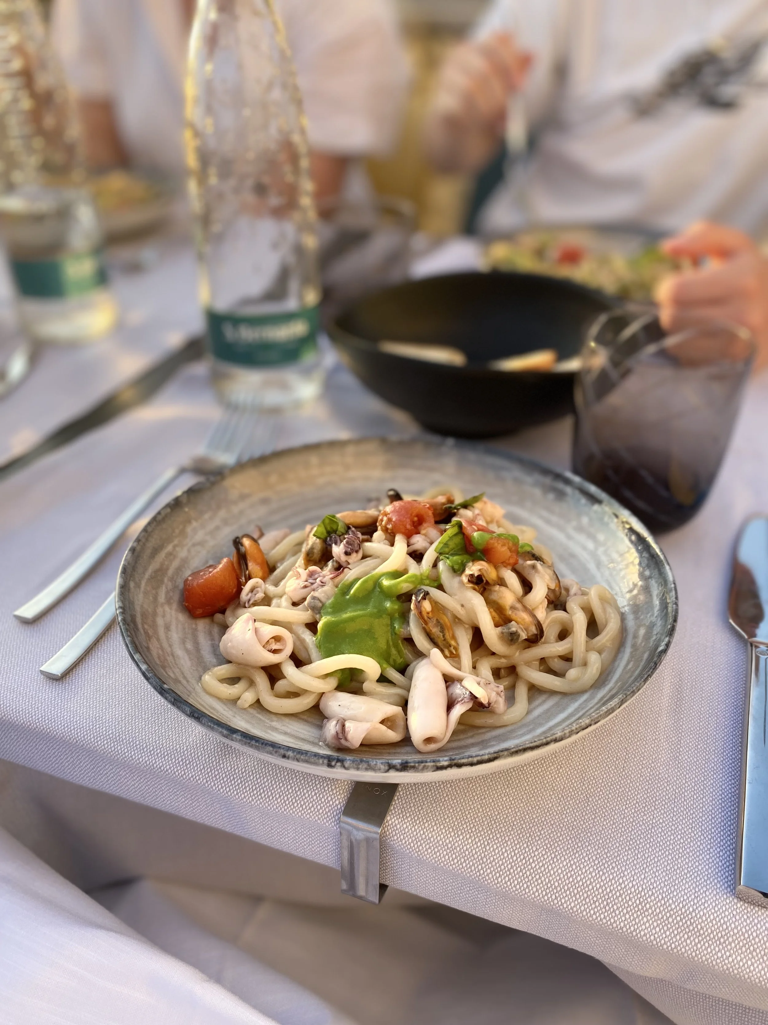 A bowl of pasta with vegetables and seafood on a table at a restaurant.