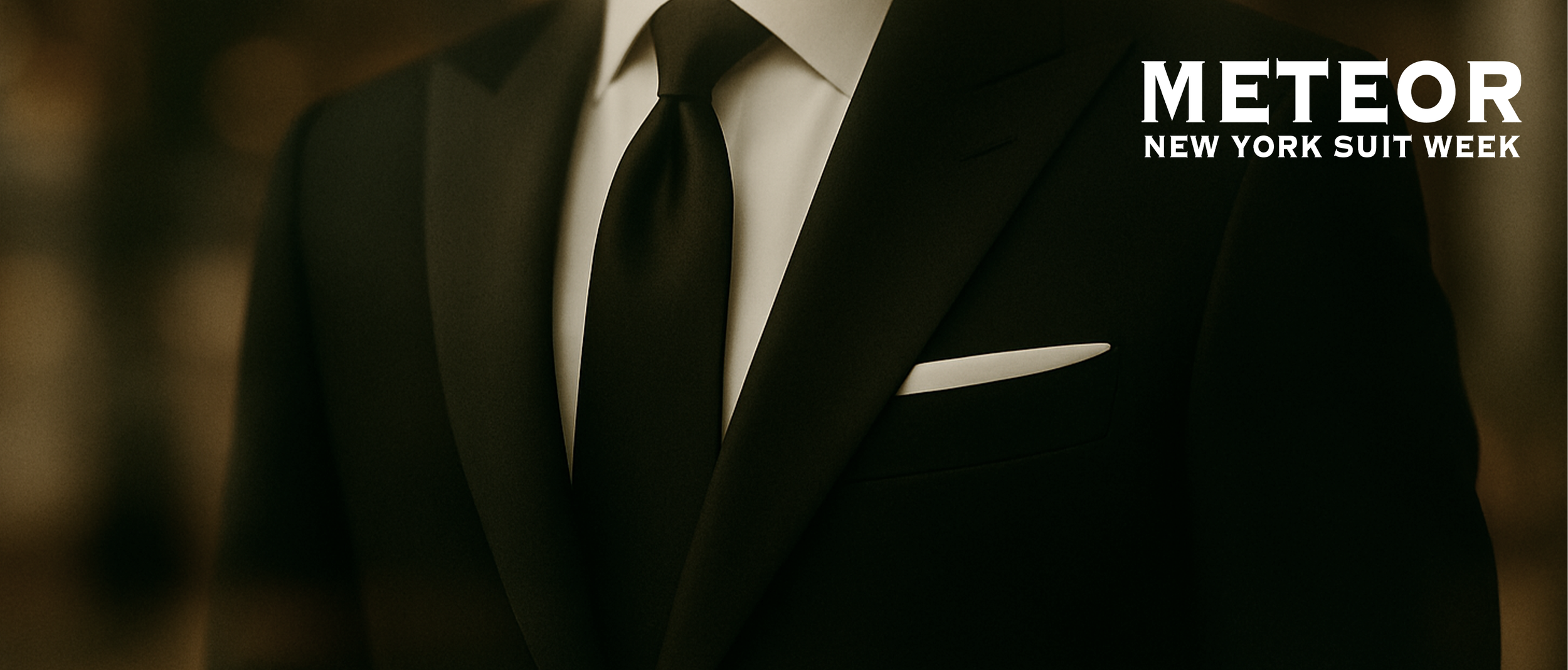 Close-up of a man dressed in a black tuxedo with a white shirt and black tie, featuring a white pocket square, with the text 'Meteor New York Suit Week' in the upper right corner.