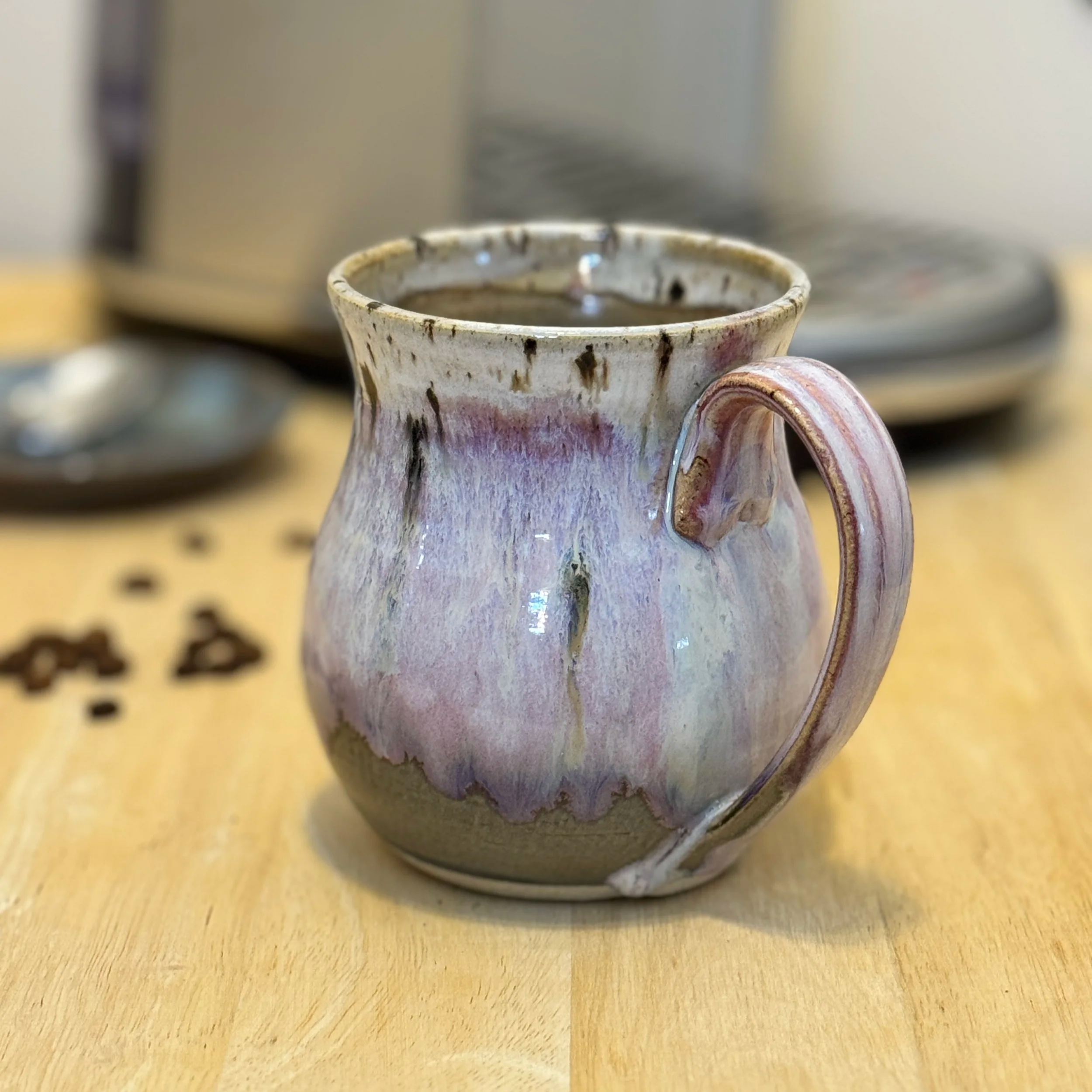 A ceramic mug with a glaze in shades of purple, beige, and white sitting on a wooden surface.