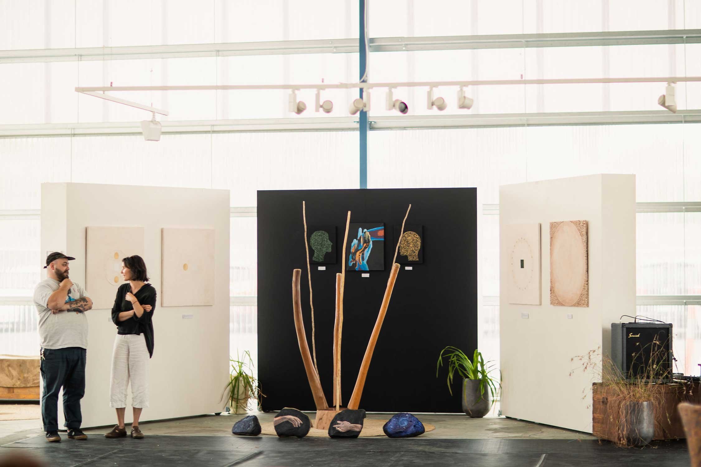 Two people speaking in front of art display featuring artwork