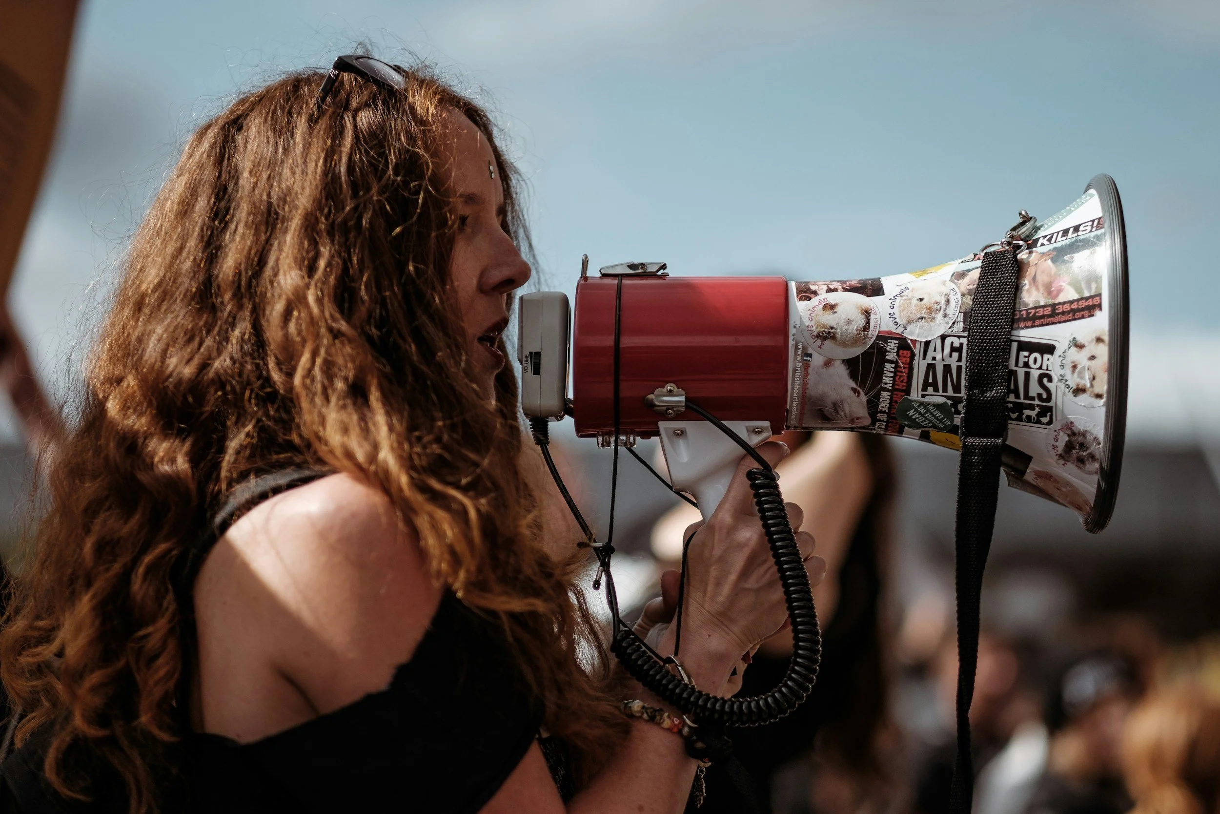 A woman with curly red hair speaking into a megaphone at an outdoor event.