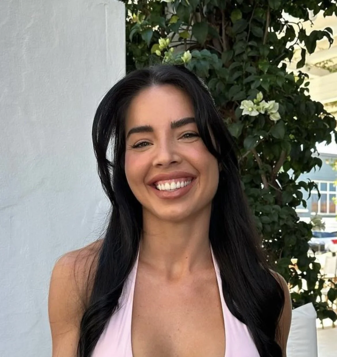 Smiling woman with long hair in front of leafy background.