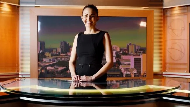 Person standing behind a news desk in a television studio.