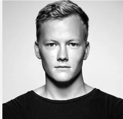 Black and white portrait of a man with short hair and a neutral expression, wearing a dark shirt.