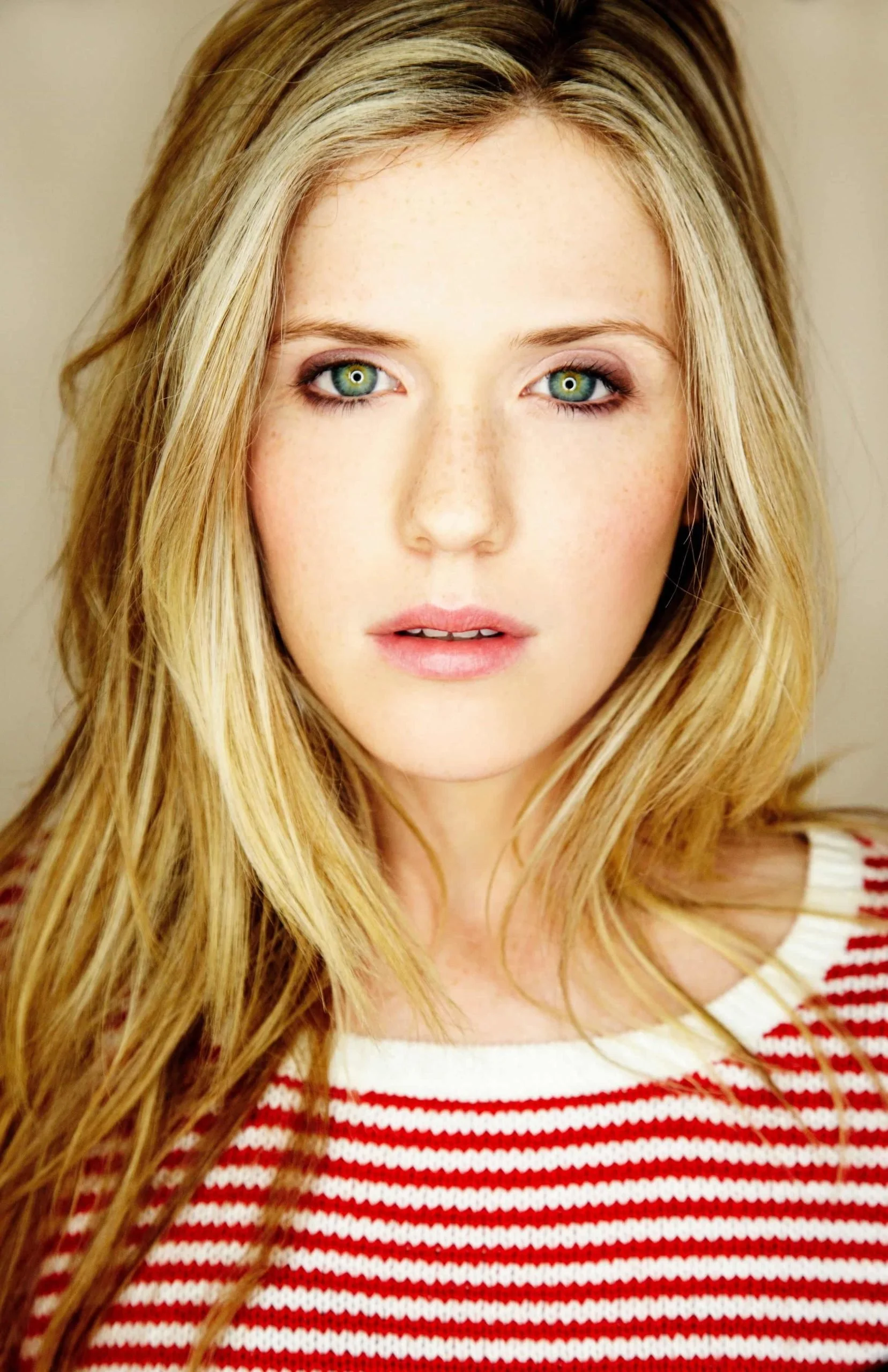 Close-up of a woman with long blonde hair, wearing a red and white striped sweater, looking directly at the camera.