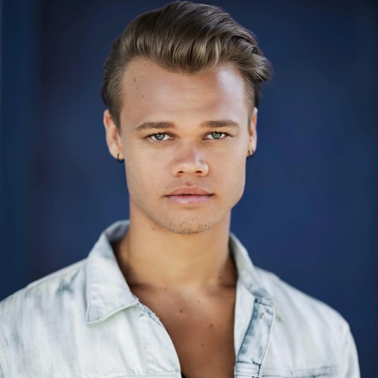 Young man with light brown hair and blue eyes wearing a denim jacket.