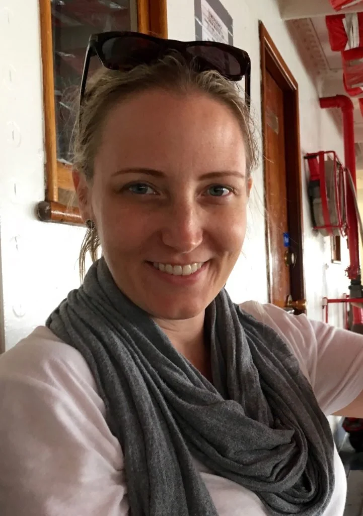 Woman smiling indoors wearing a gray scarf and sunglasses on her head.