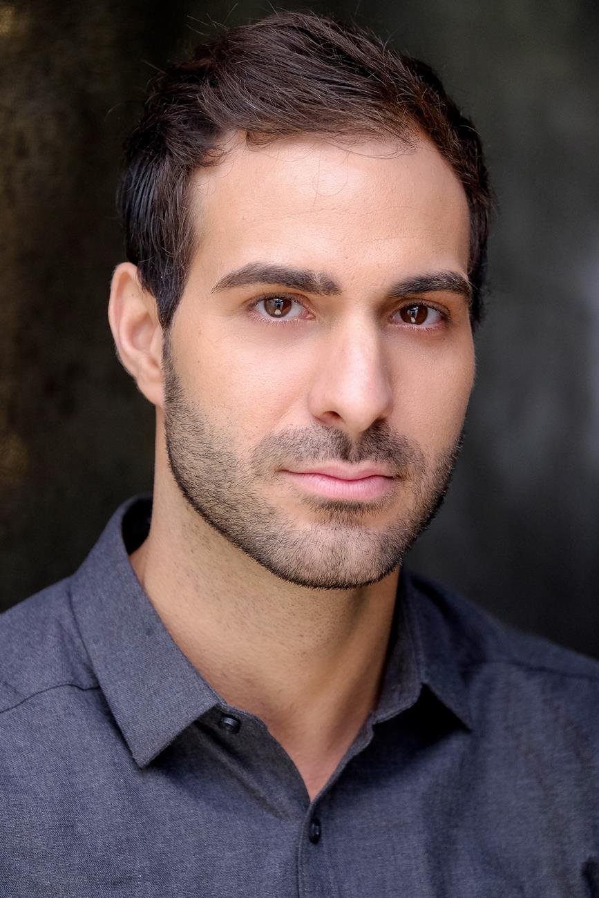 Portrait of a man with short dark hair and a beard, wearing a gray shirt.