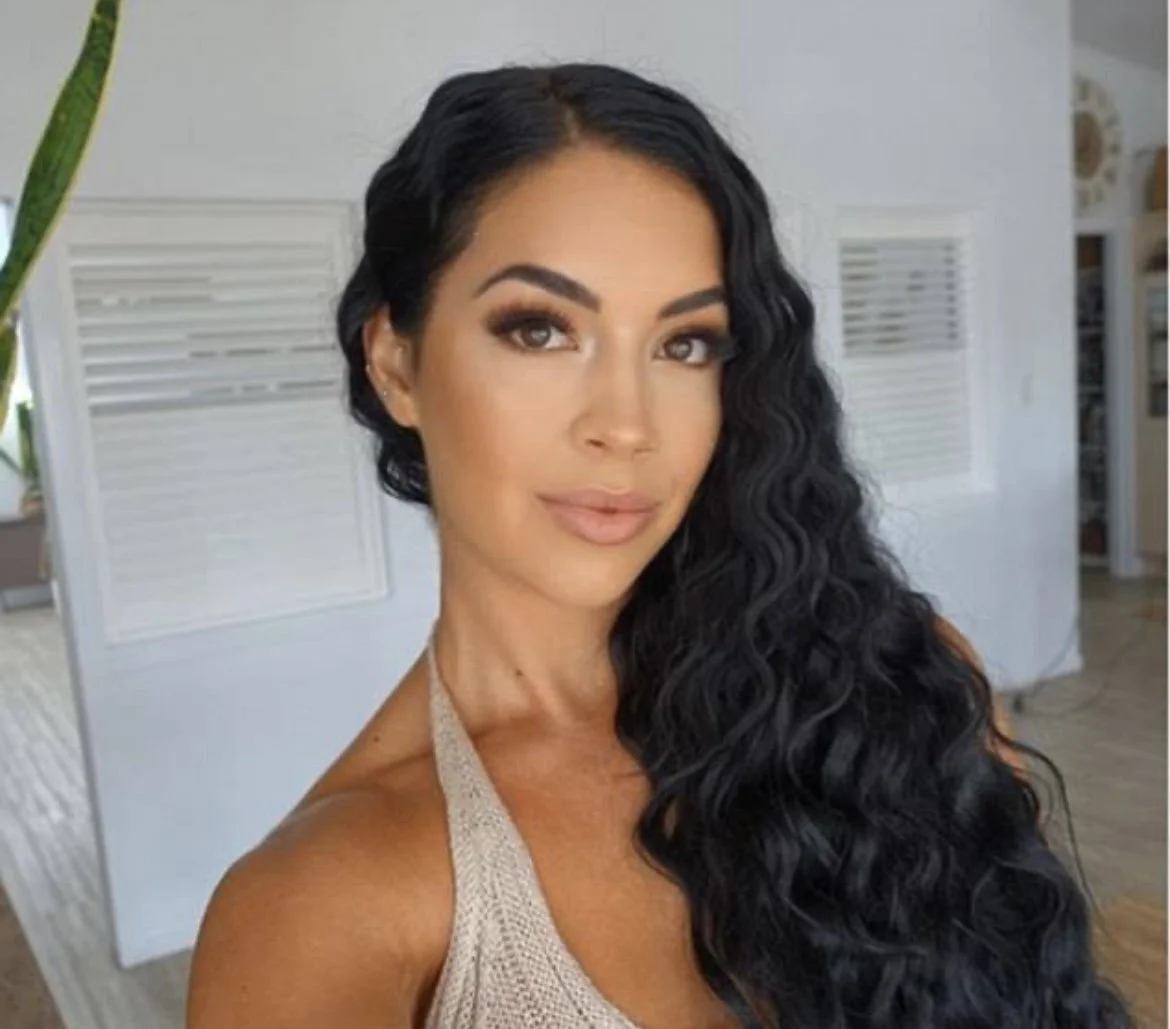 Person with long wavy hair and a neutral top posing indoors.