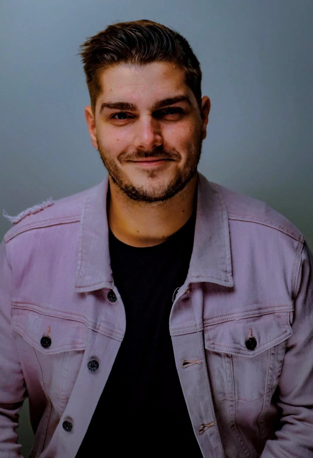 Portrait of a smiling man wearing a light-colored denim jacket against a neutral background.