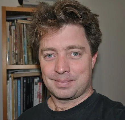 Man in front of a bookshelf, smiling