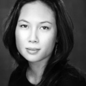 Black and white portrait of a woman with long hair, wearing a dark top, looking directly at the camera.