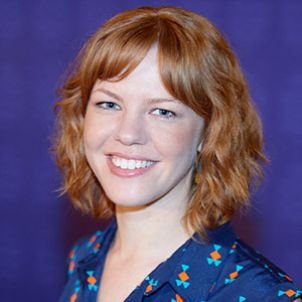 A person smiling in front of a purple background, wearing a blue shirt with colorful patterns.