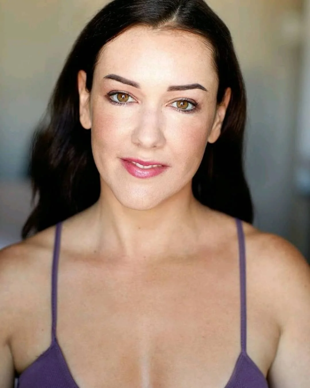 Woman with dark hair wearing a purple top, looking at the camera.