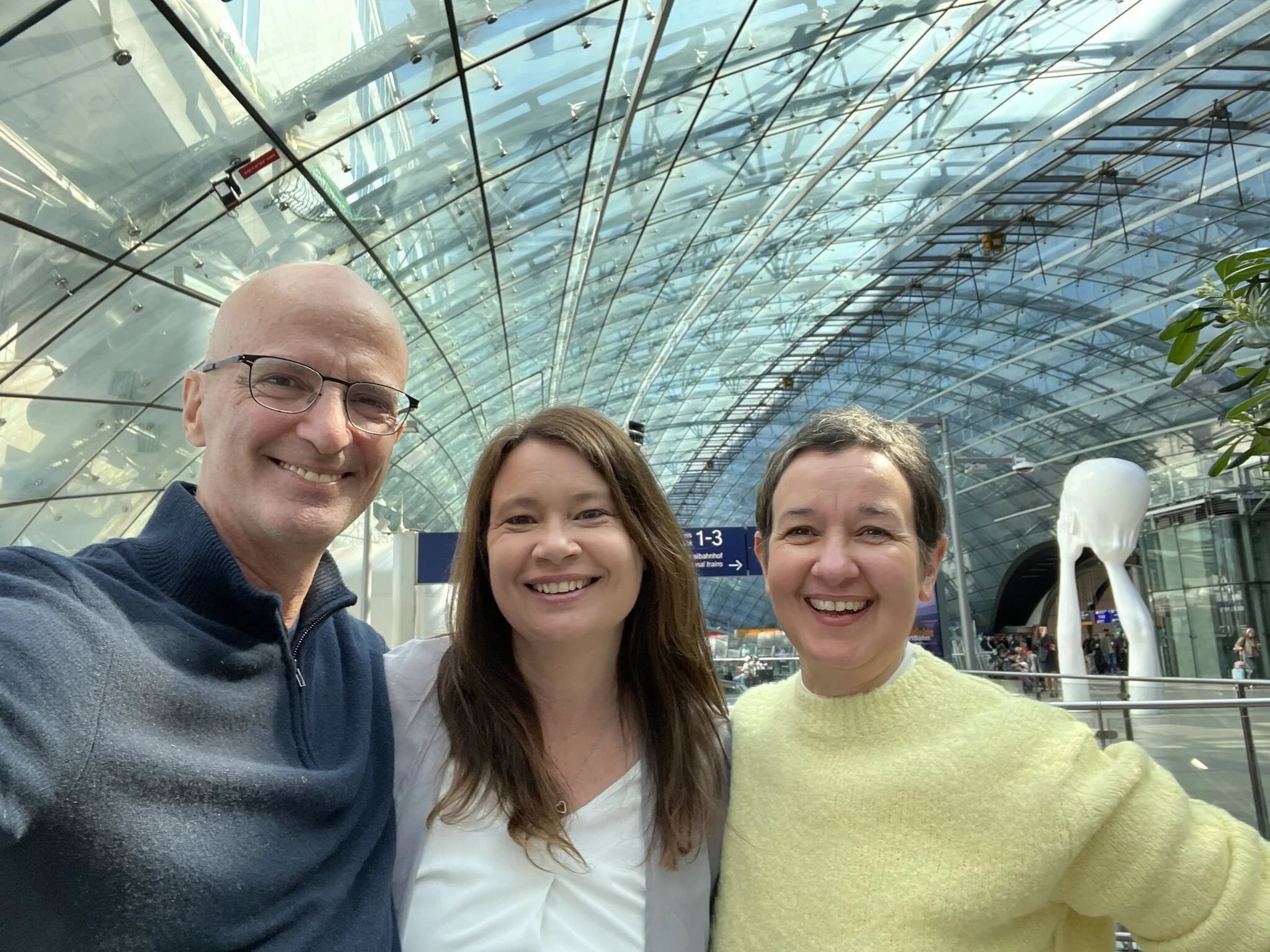 John Stepper with Bettina Jung and Constanze Zeller smiling together in the glass atrium of Frankfurt Airport.