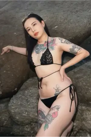 Девушка из Паттайи позирует на скалистой местности, демонстрируя свои татуировки на фоне природы.