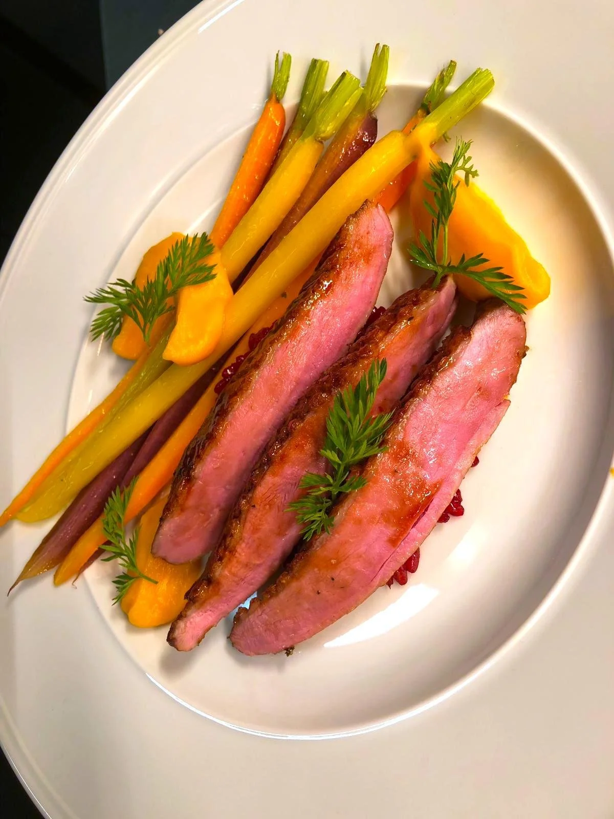 Gekookte of gestoomde groenten, inclusief wortelen en gele asperges, geserveerd met gesneden eendenborst en verse kruiden op een wit bord.