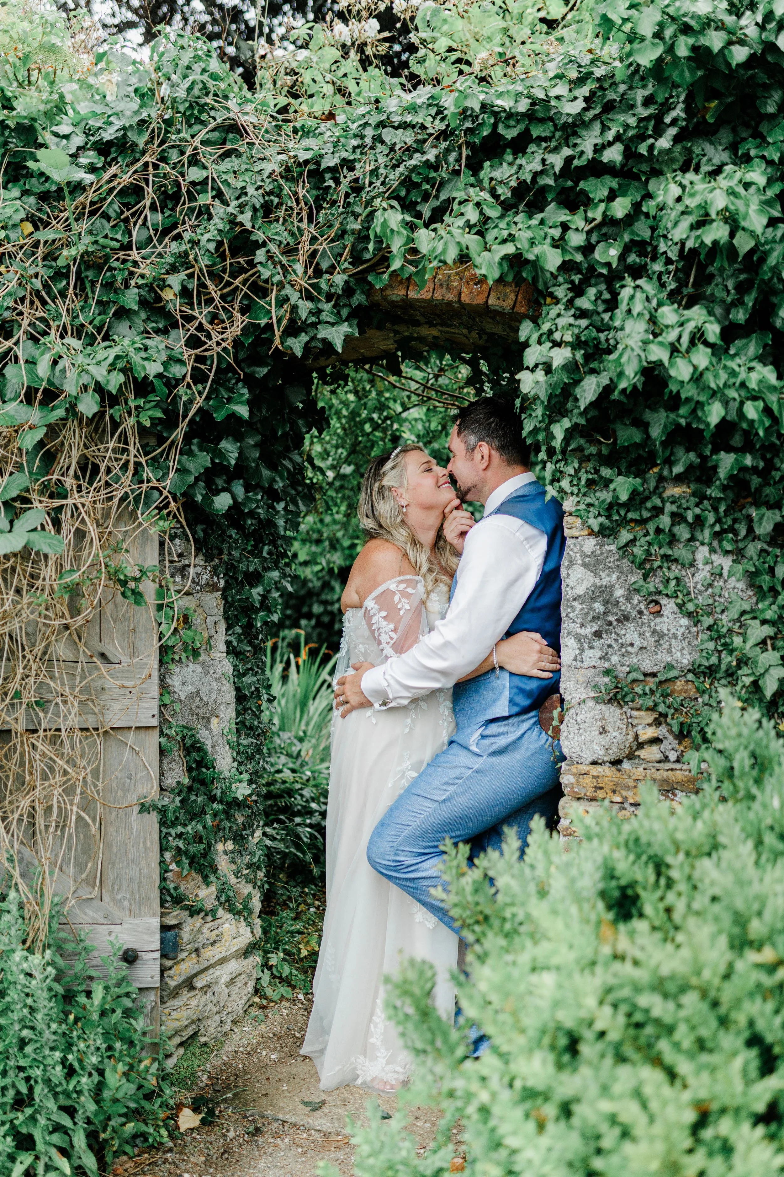 Bride and groom cuddling under walled garden archway at Carwinion House