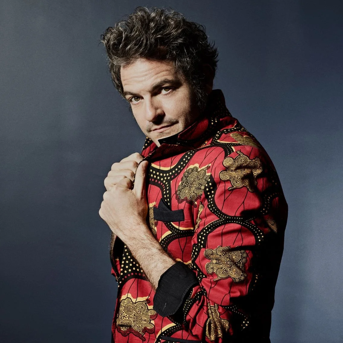 Homme portant une veste colorée, posant dans un studio avec un arrière-plan neutre.