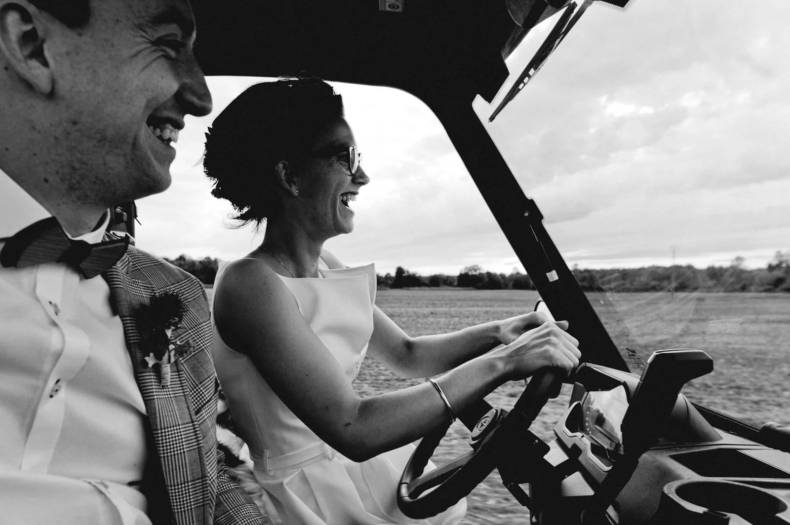 Un couple souriant dans une voiturette de golf, la femme conduisant dans un champ, en noir et blanc.