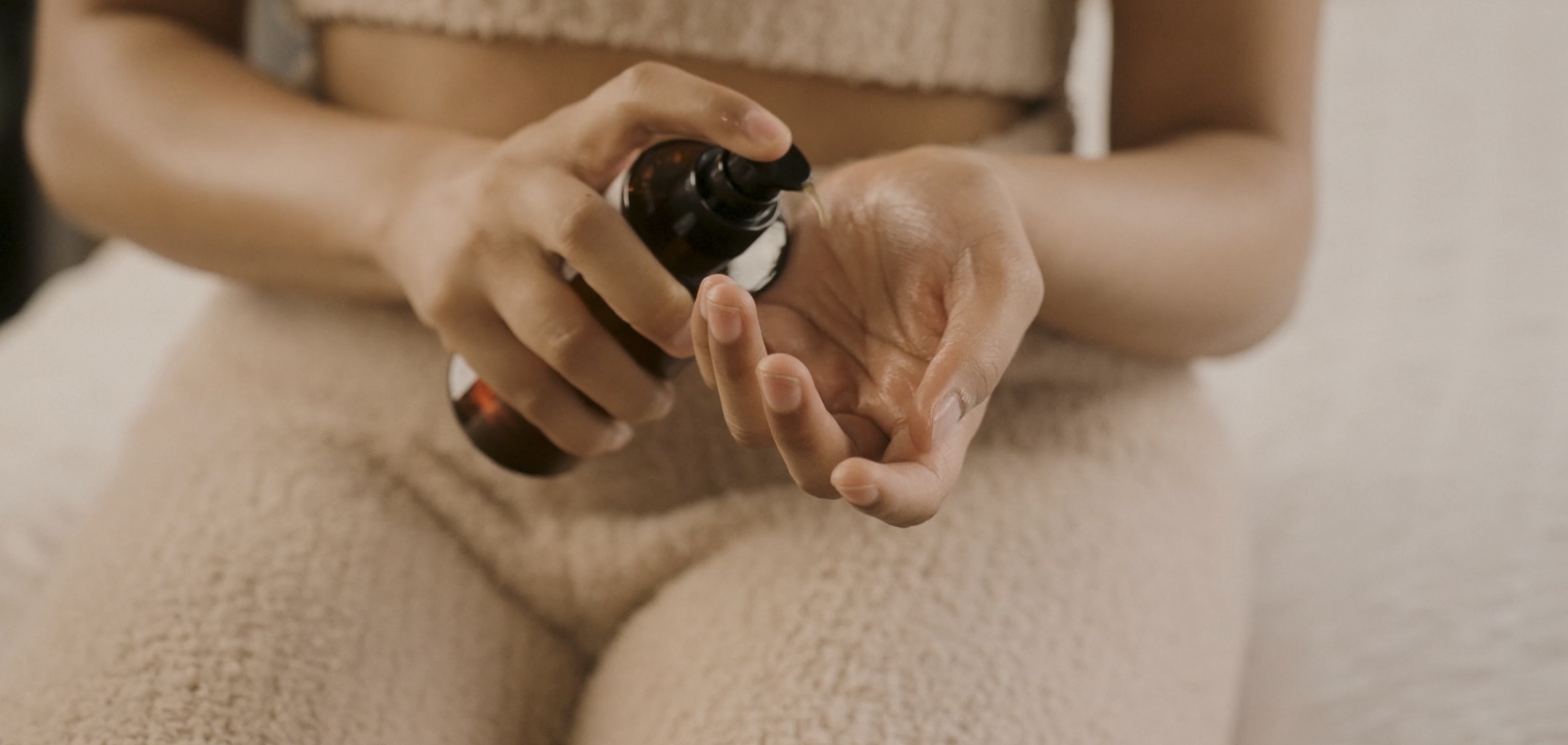 Person applying lotion or cream to their hand from a brown bottle.