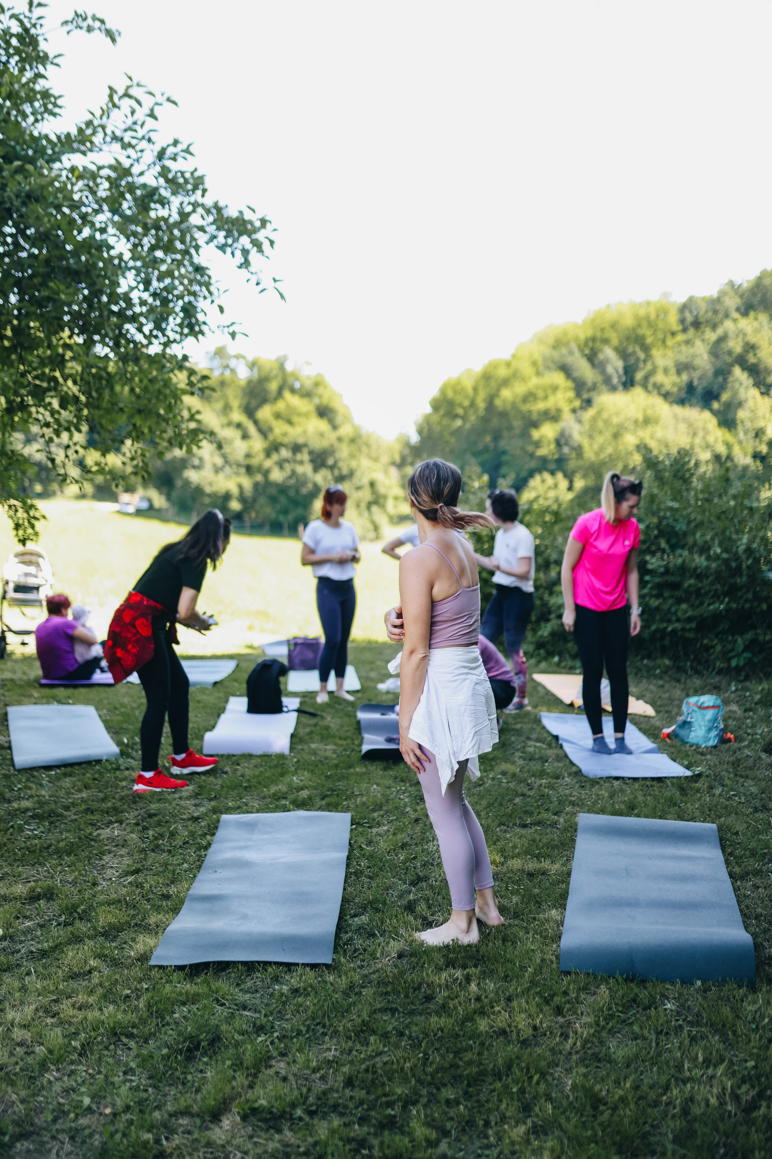 Group of women practicing outdoor yoga on mats in a grassy park surrounded by trees on a sunny day.