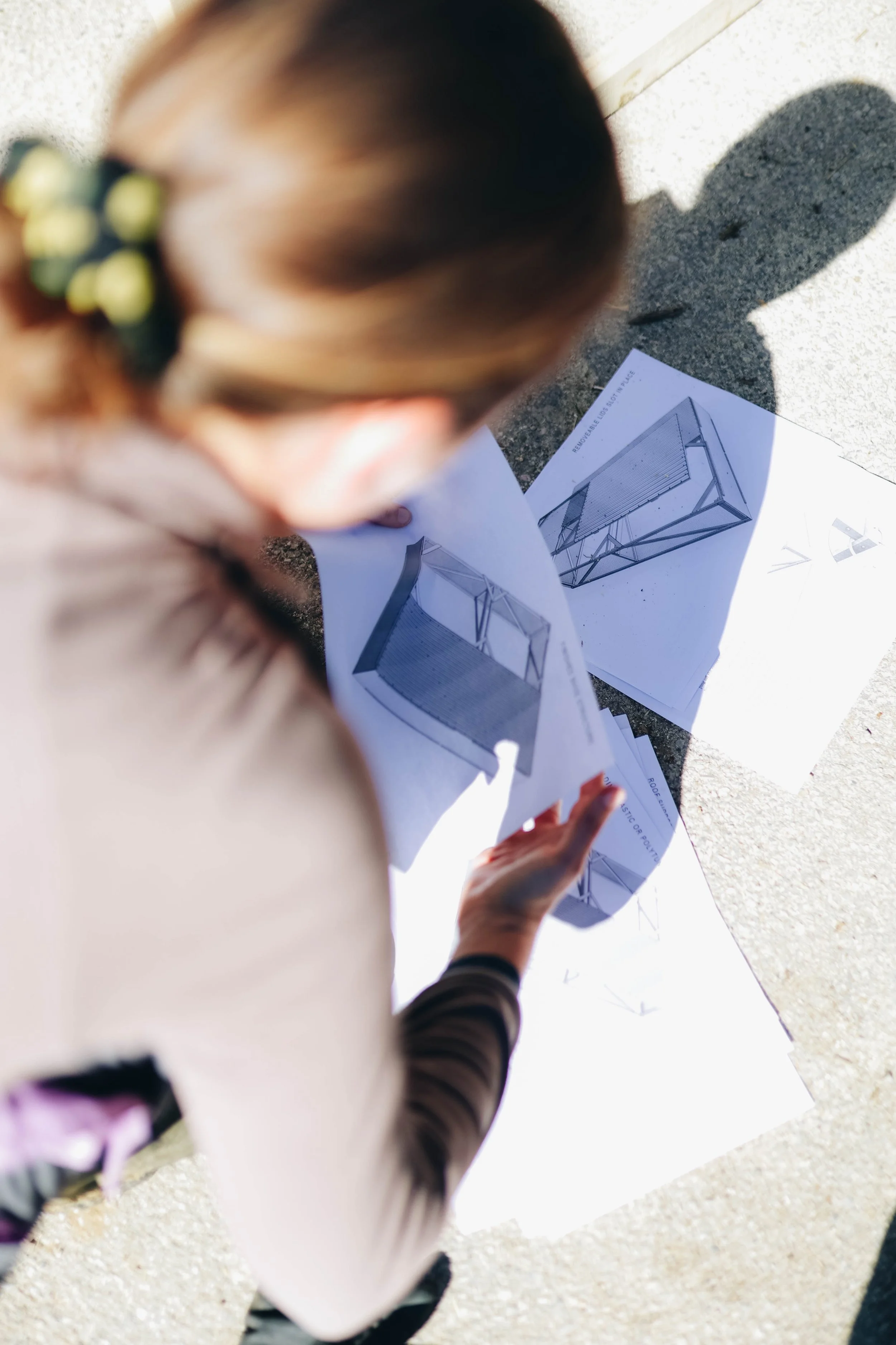 A person looking at architectural blueprints on the ground outside in sunlight.