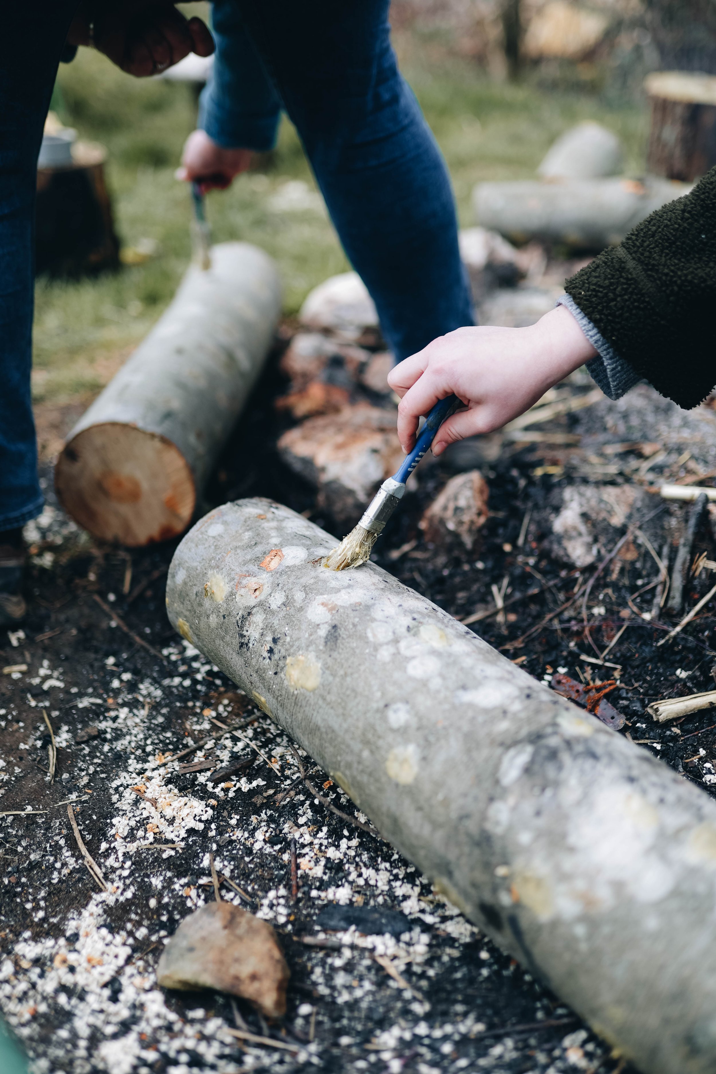 People carving designs into logs with brushes outdoors.