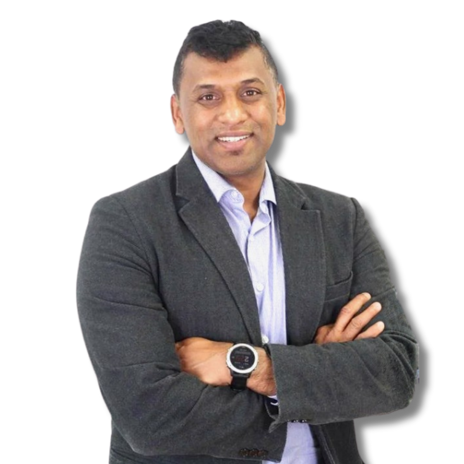 A man with short black hair, wearing a dark gray blazer, light blue shirt, and a wristwatch, standing with arms crossed and smiling at the camera against a plain white background.