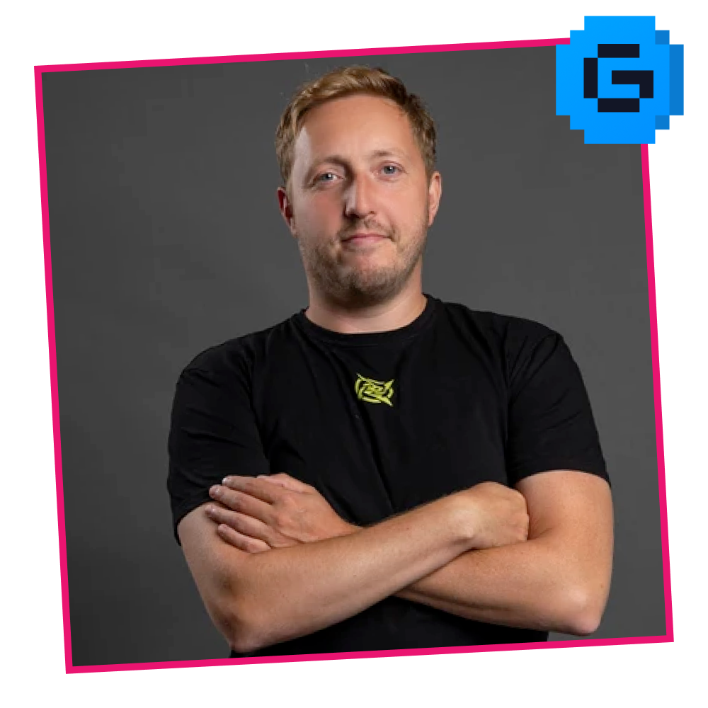 Portrait of a man with crossed arms against a gray background, wearing a black t-shirt with a yellow logo, with a pink border and a blue pixelated icon in the top right corner.