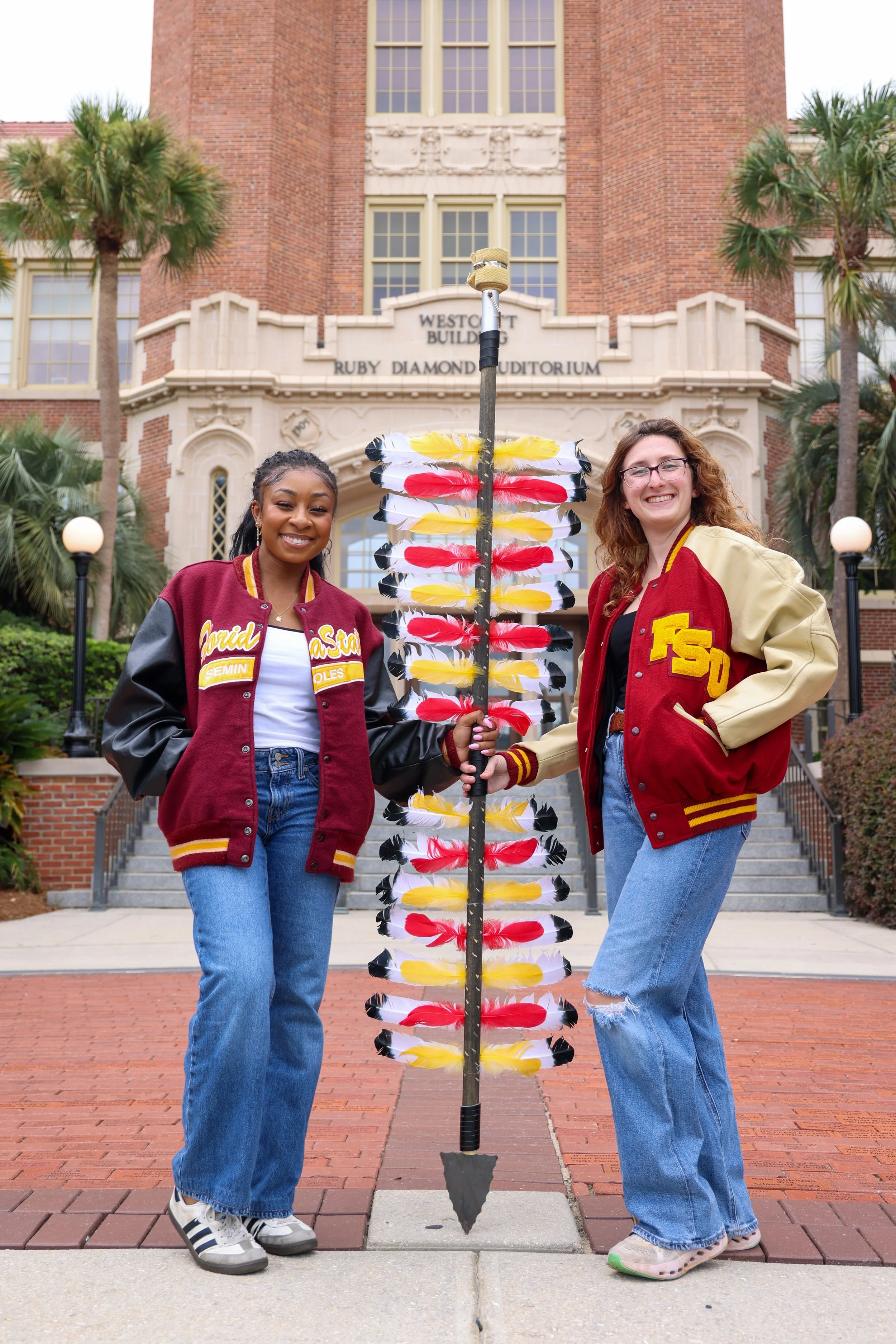 Person in a graduation cap drinks from a bottle in front of the Florida State University sign at DeVoe L. Moore University Center.