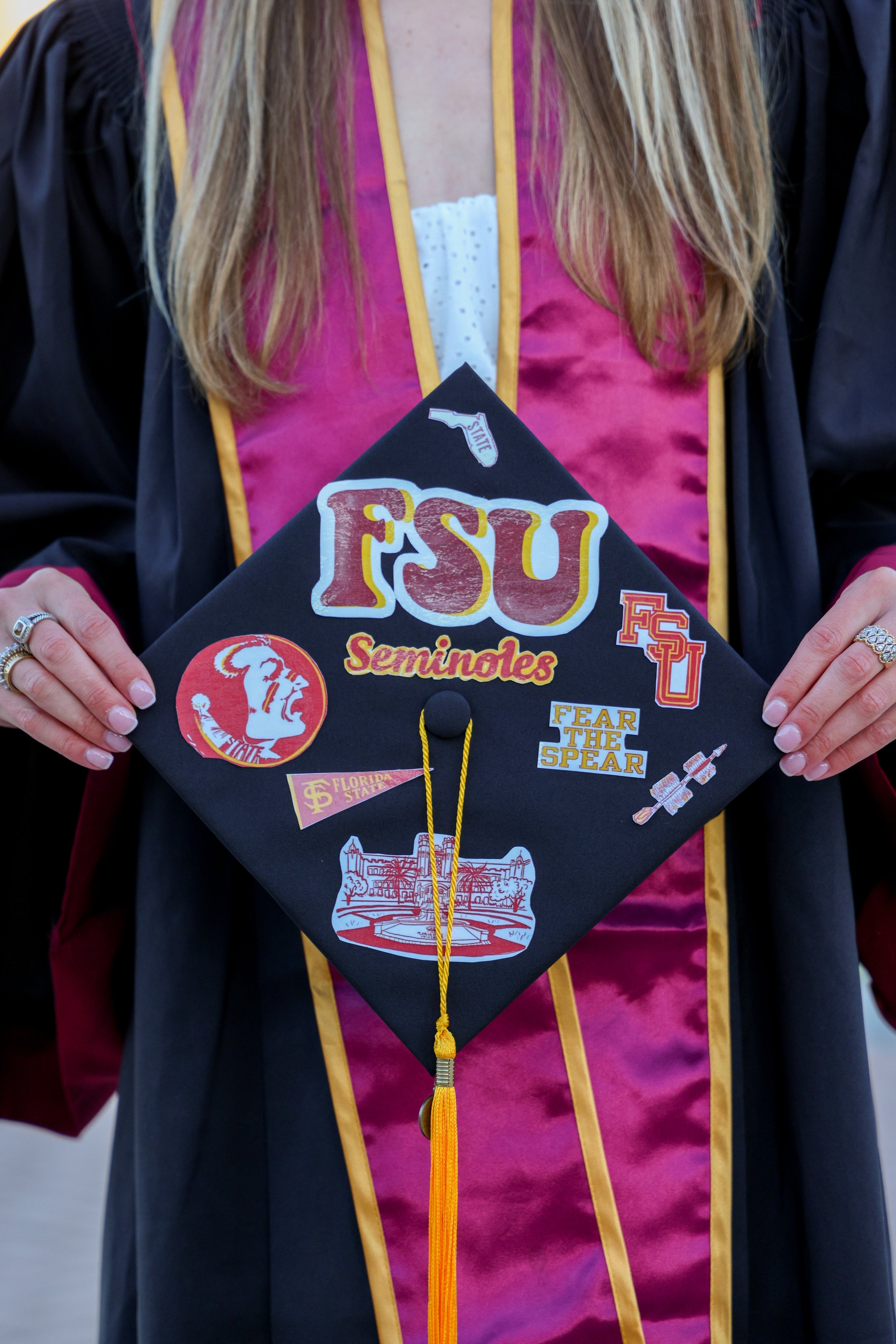 Person in a graduation cap drinks from a bottle in front of the Florida State University sign at DeVoe L. Moore University Center.