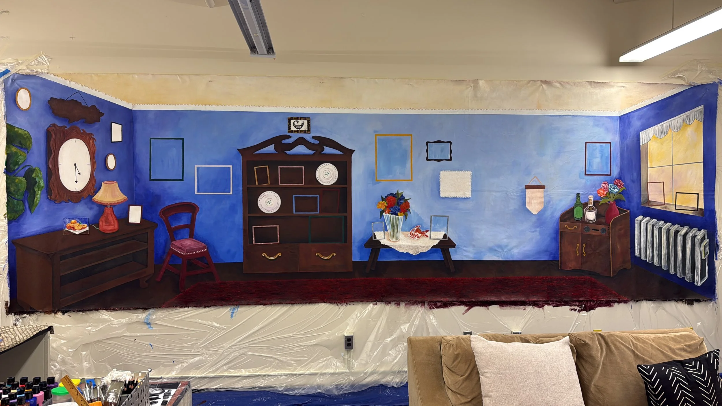 Photograph of the home places mural. There is a shelf, a table, and various photo frames.