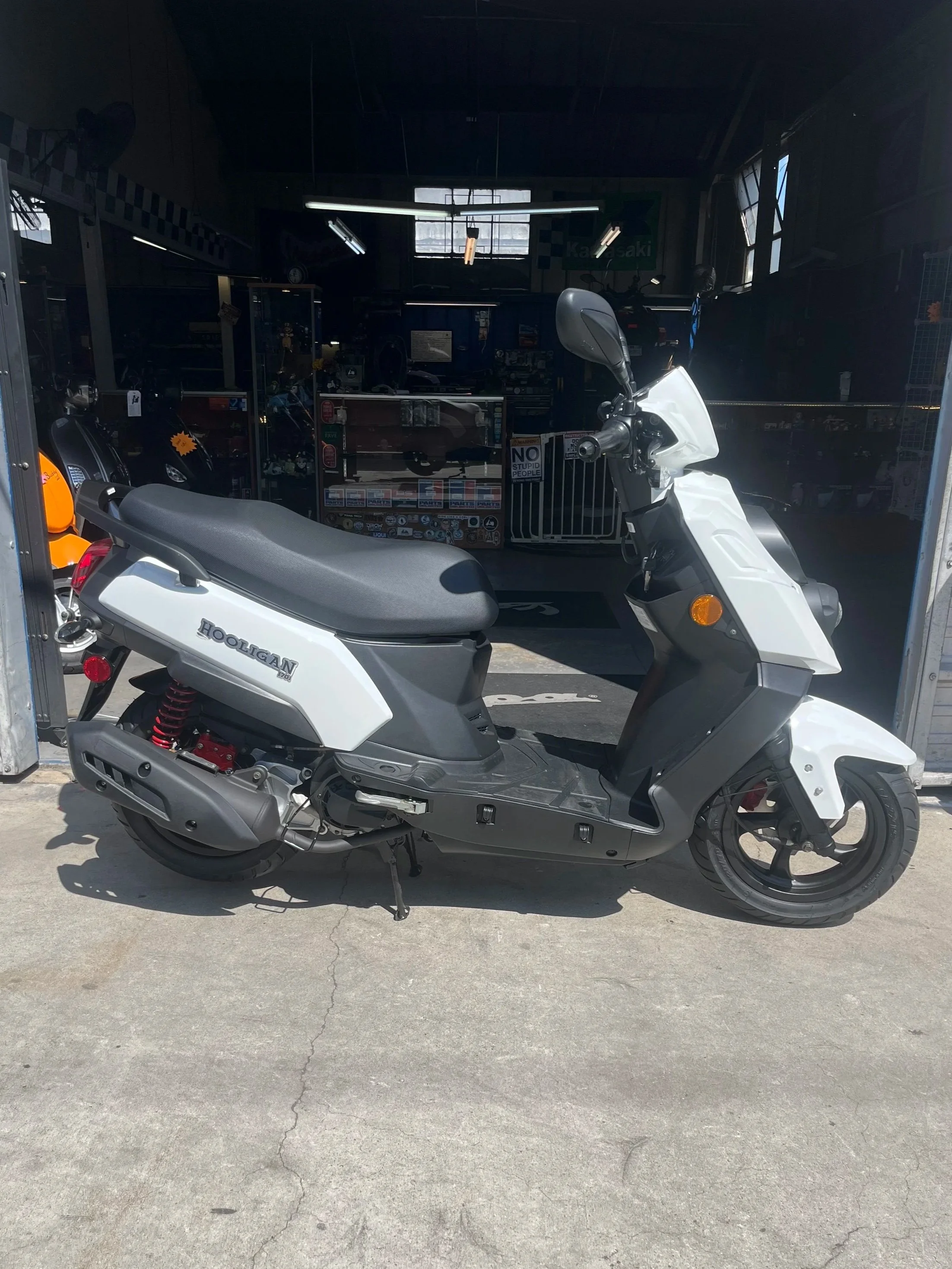 A white and black motor scooter parked outside a shop with a garage interior visible in the background.