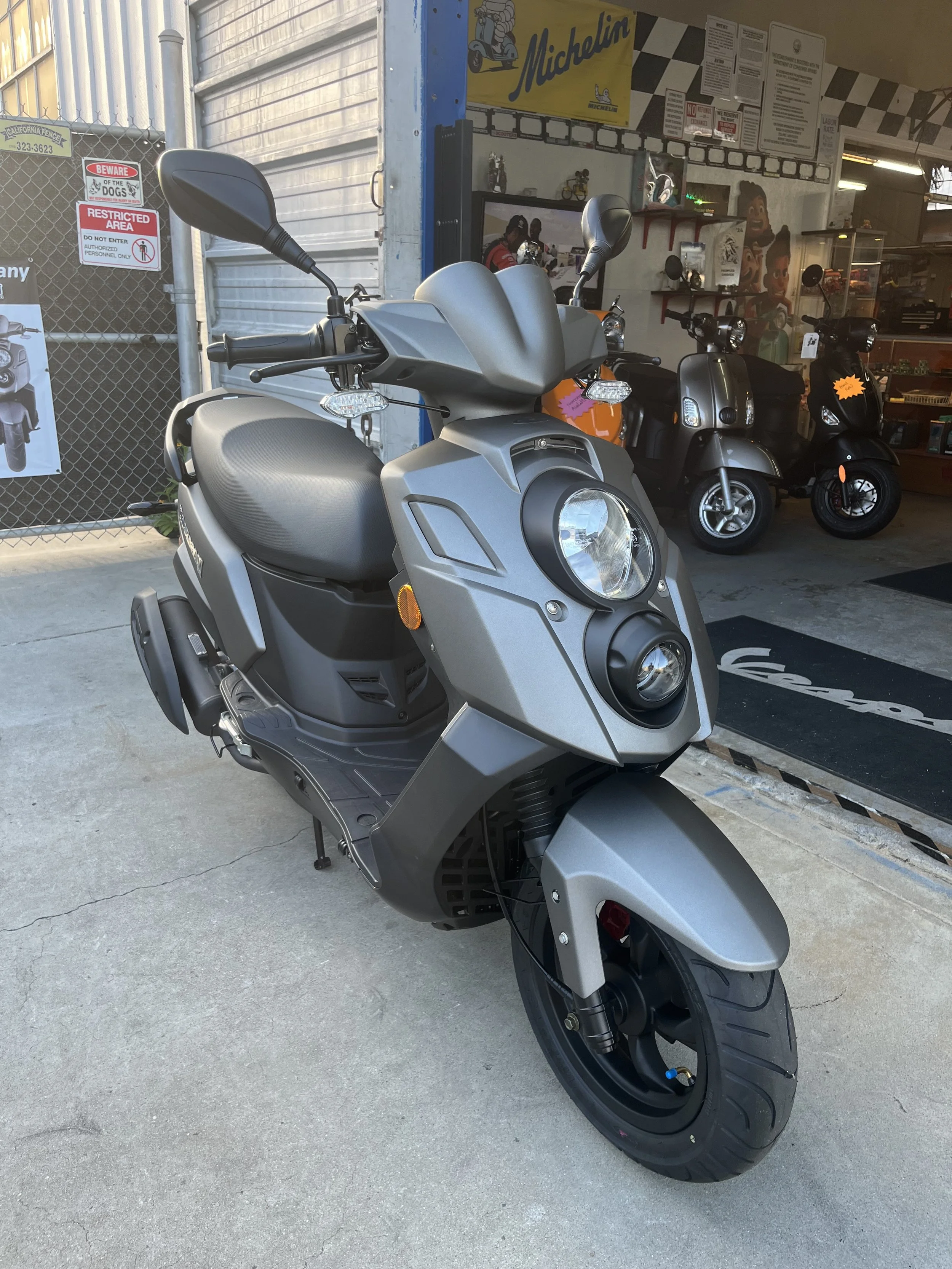 A silver electric scooter parked outside a store with other scooters in the background.