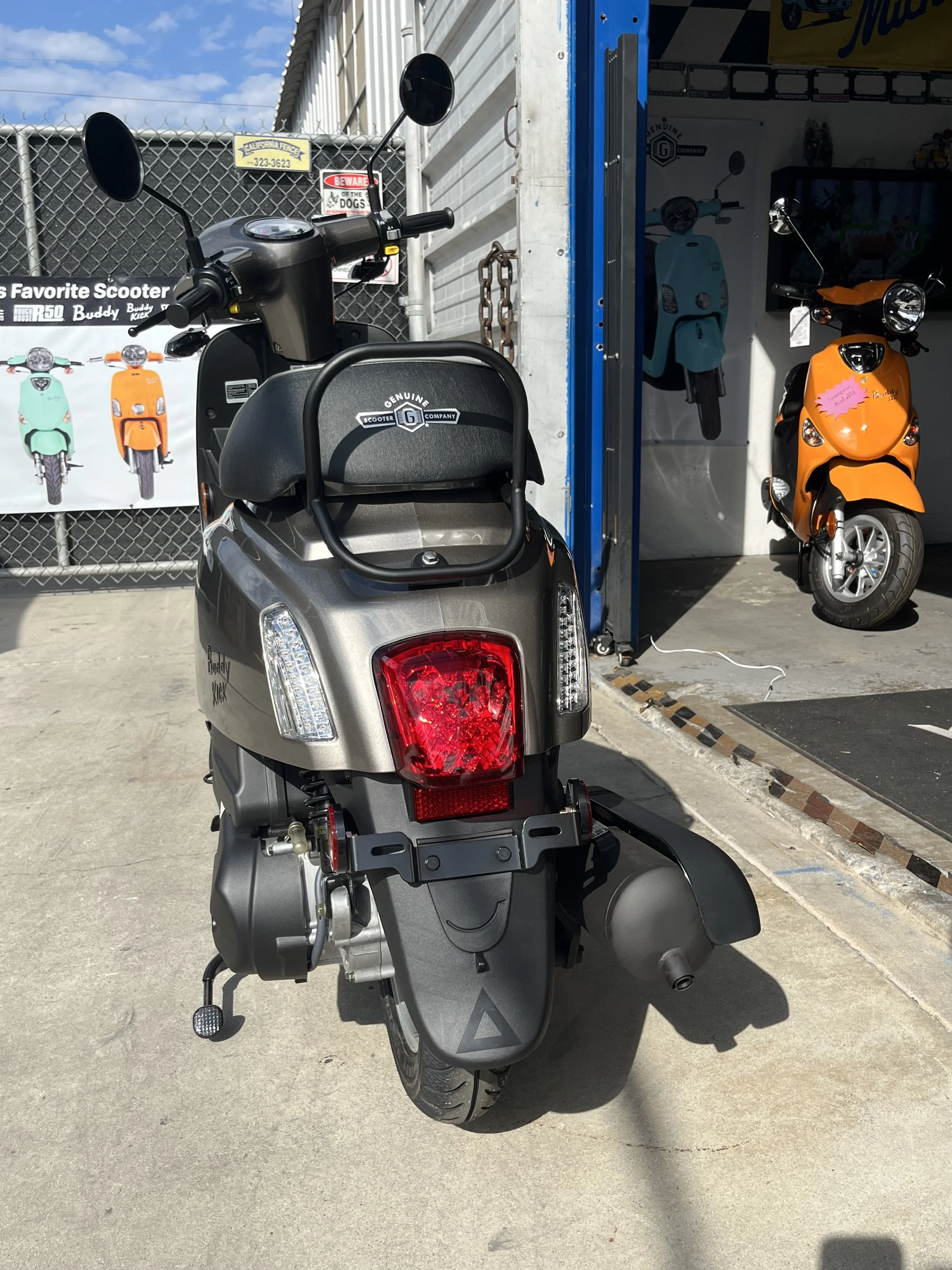 Glossy Titanium scooter parked outside a scooter shop with colorful scooters in the background.