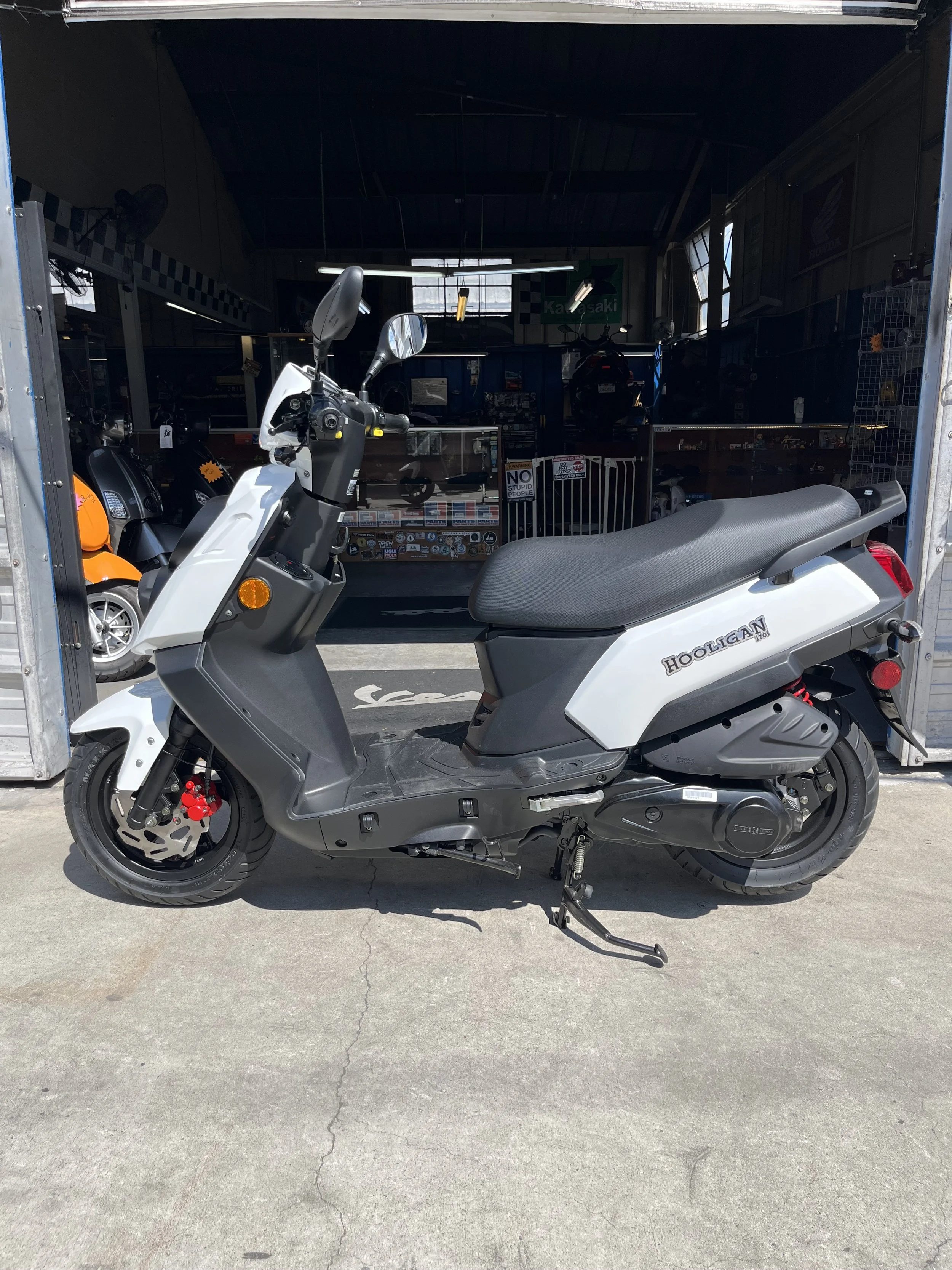 White and black scooter parked outside a store with a motorcycle shop visible in the background.