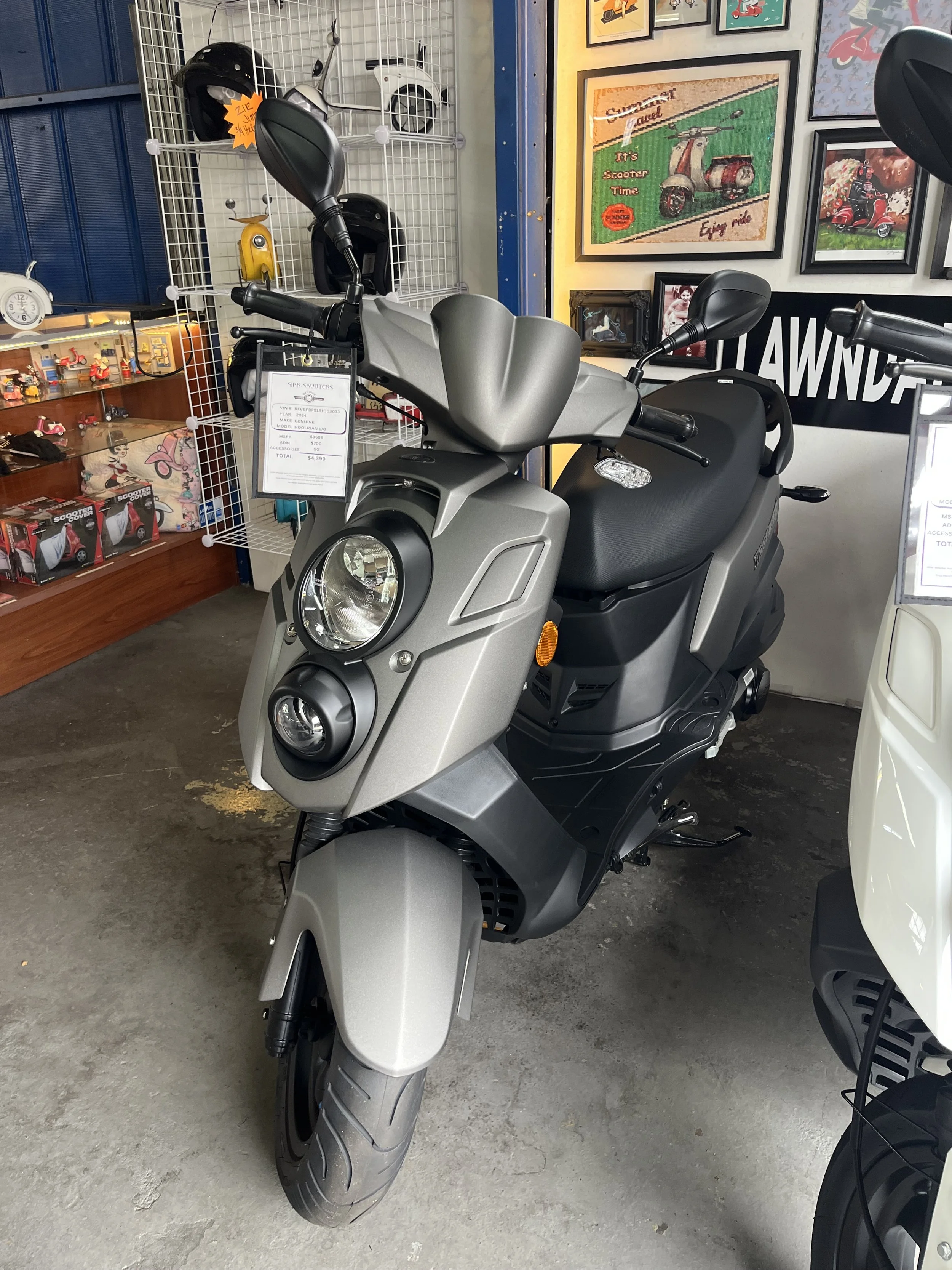 Gray electric scooter on display at a store, with framed pictures and helmets in background.