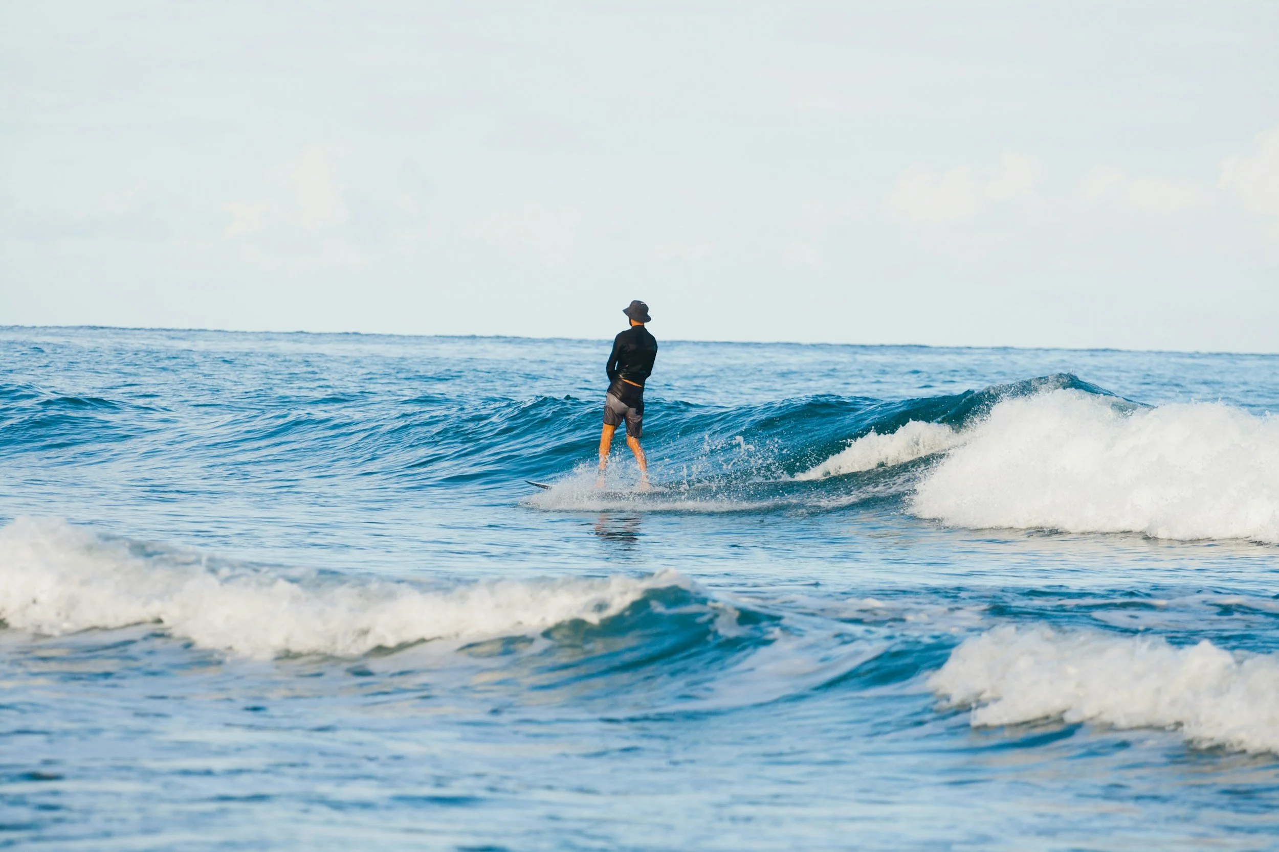 A person standing on a surfboard in the ocean, facing the horizon, with waves around.