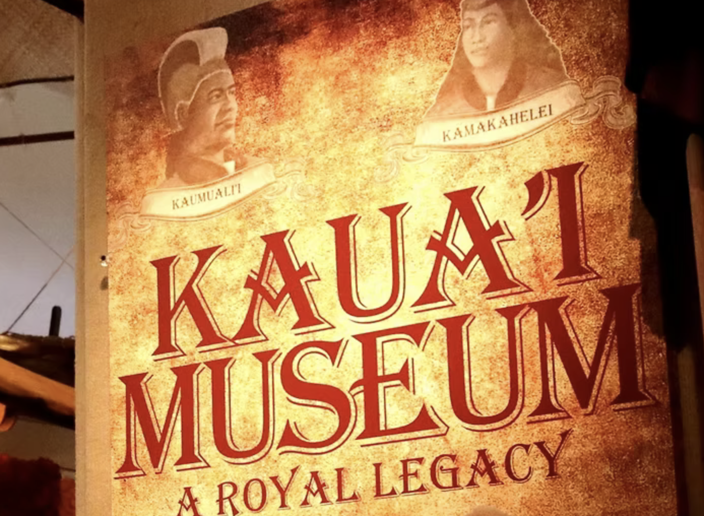 A poster for the Kaunai Museum featuring two portraits of figures in traditional Hawaiian attire with caption banners labeled 'Kaumuali'i' and 'Kamehameha'. The background is an orange and yellow textured design with the museum's name prominently in large red letters, and the phrase 'A Royal Legacy' beneath.