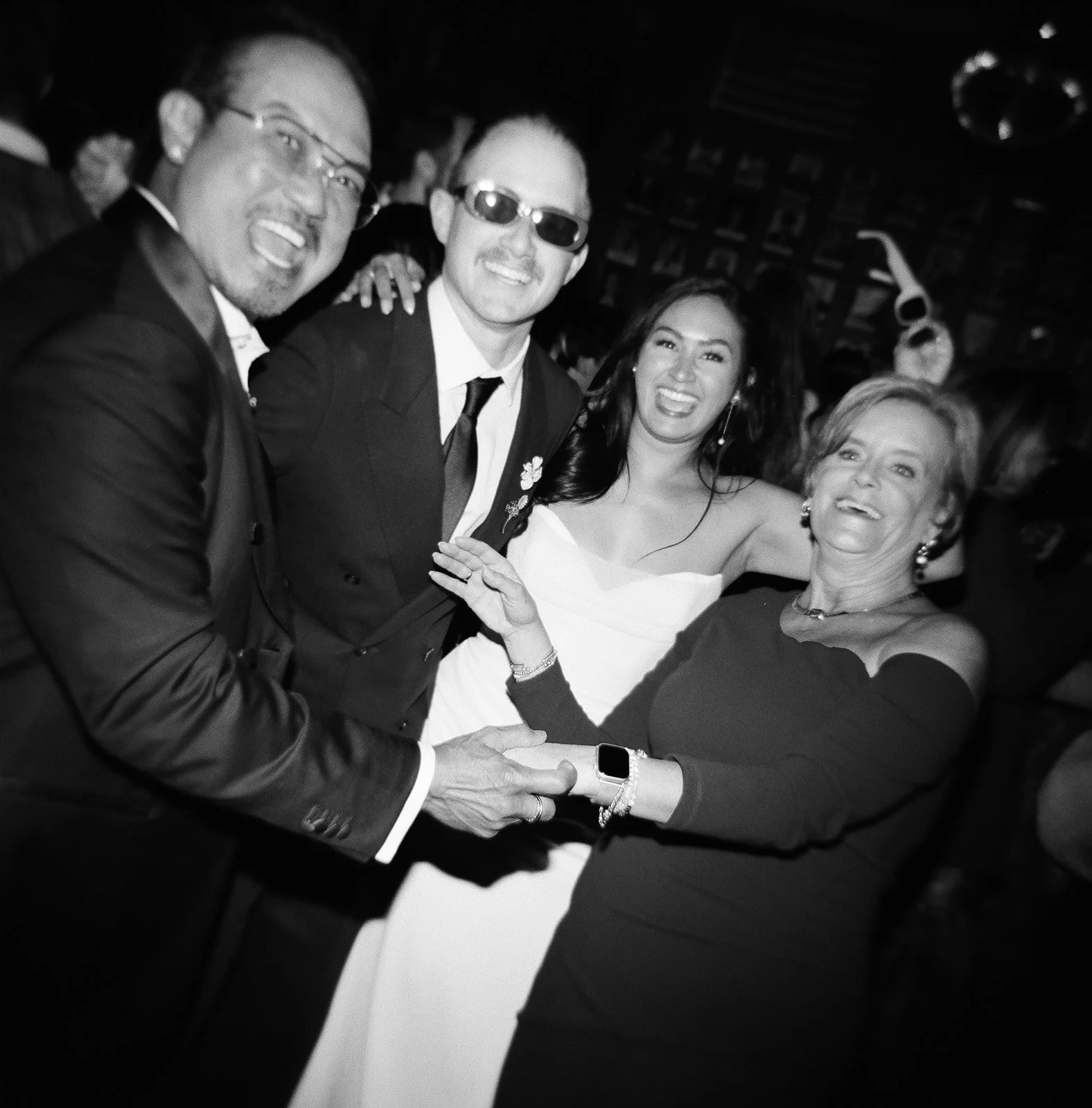 Four people dressed in formal attire smiling and holding hands, celebrating at an event.