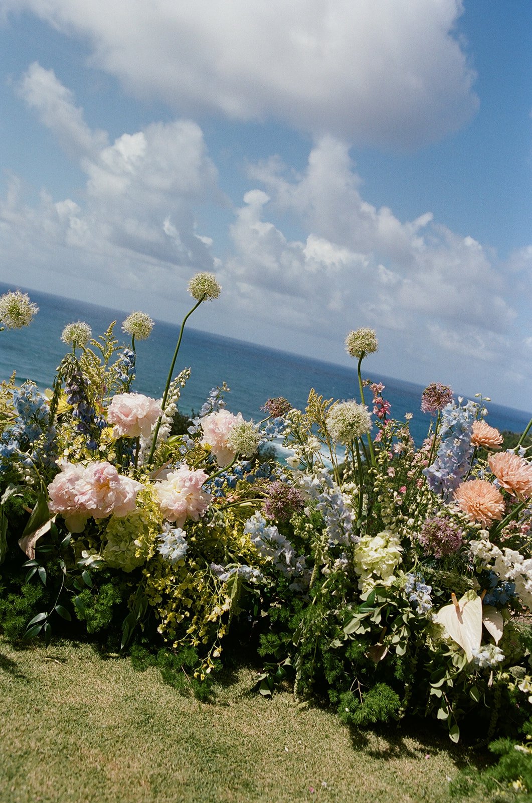 Colorful flower arrangement on grass with ocean and sky in background.