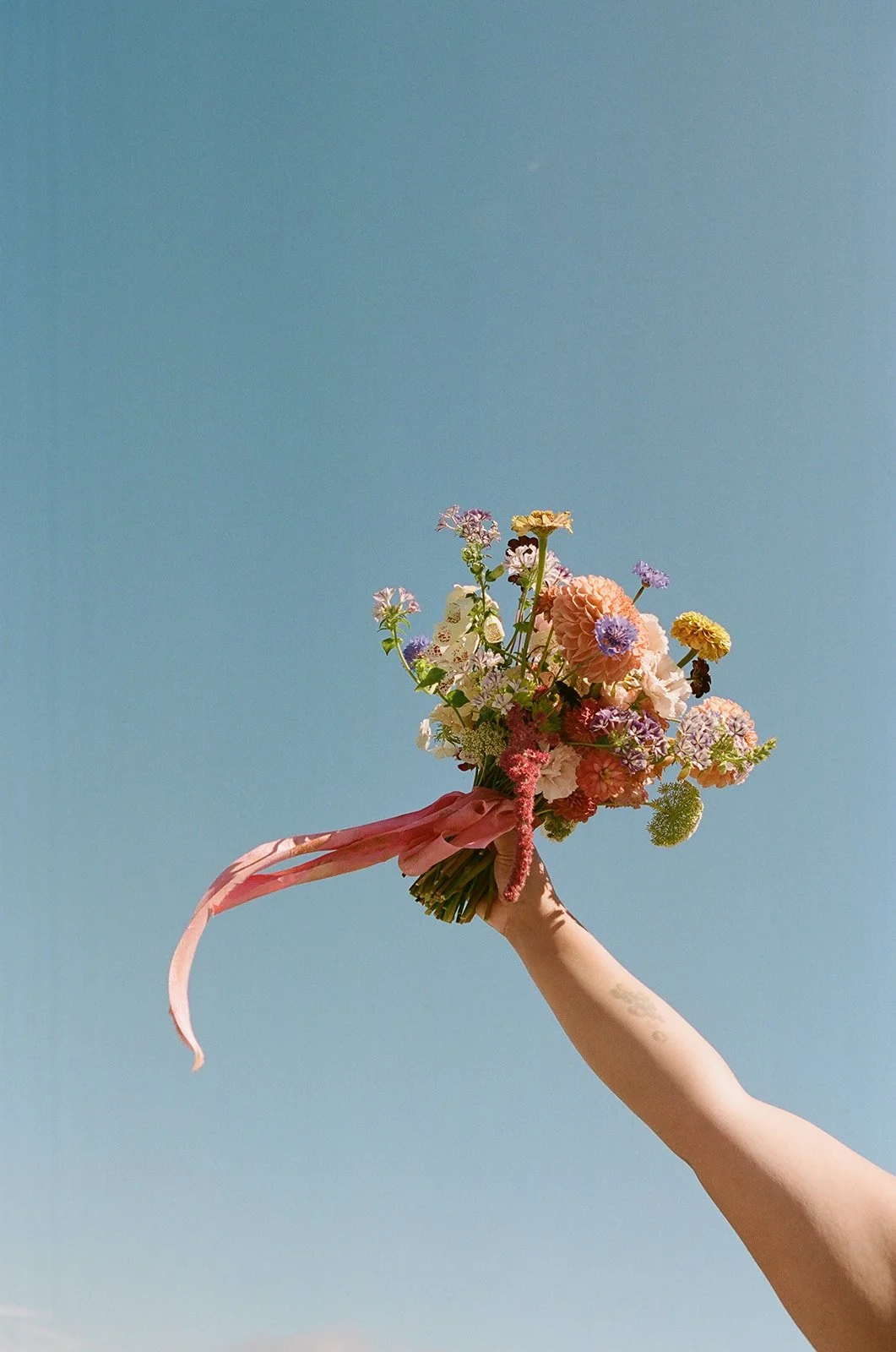A person holding a colorful bouquet of flowers against a clear blue sky.