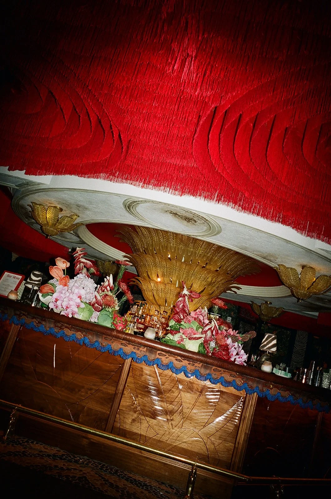 Decorative bar with floral arrangements, gold accents, and red ceiling with gold leaf designs, featuring ornate woodwork and lighting.