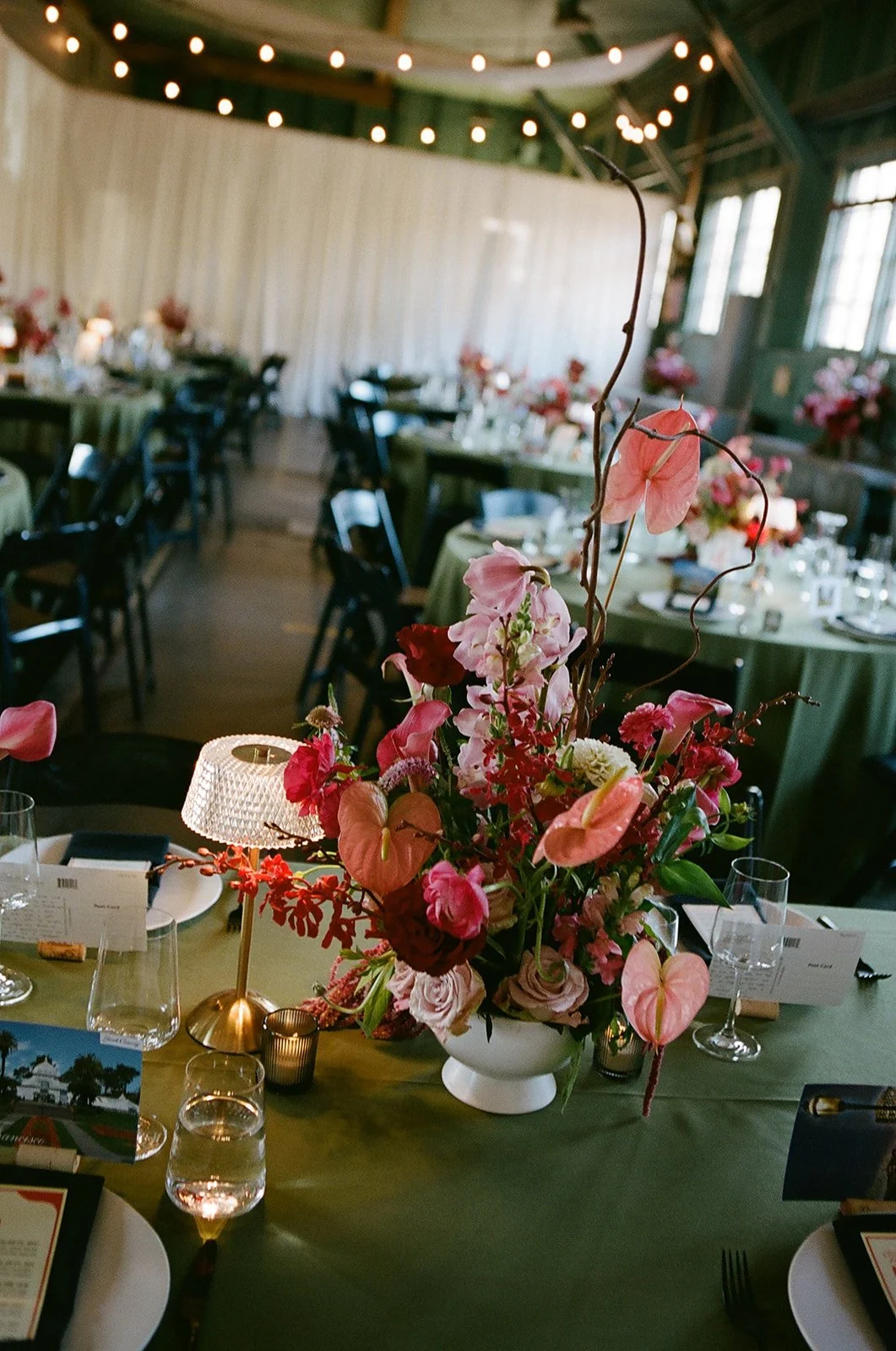 A floral centerpiece with pink and red flowers on a green-covered table at a decorated event space.
