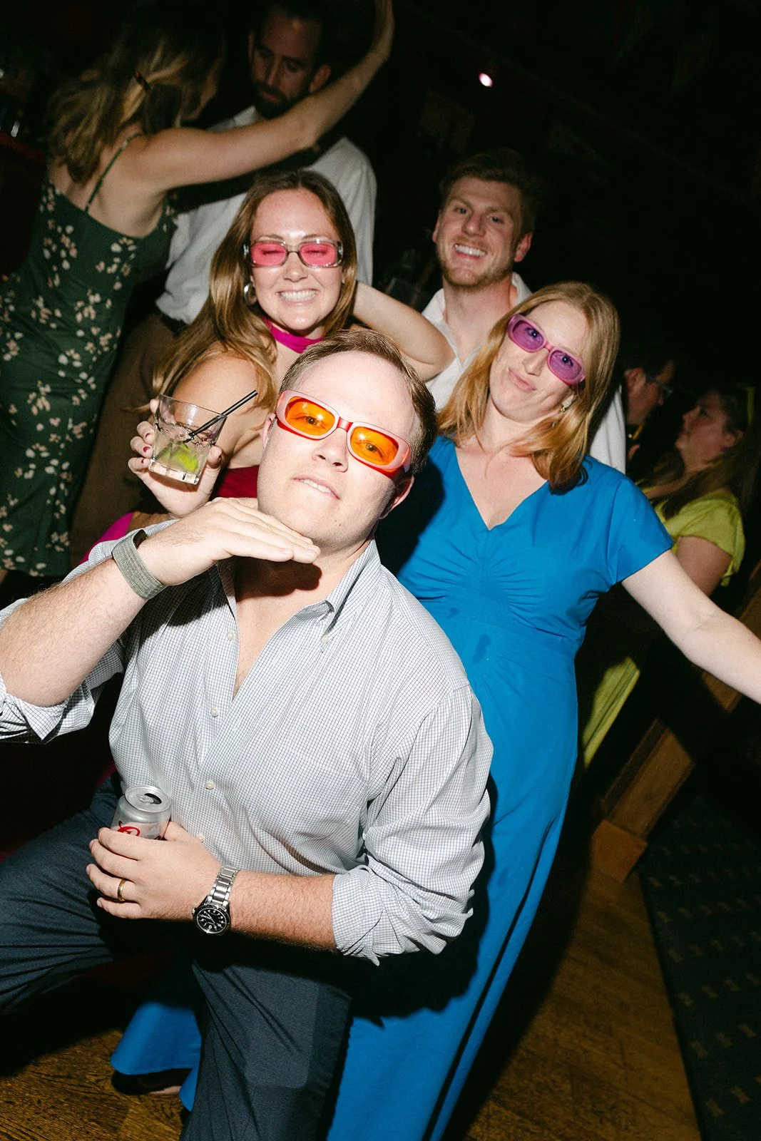 Group of people at a party wearing colorful 3D glasses, with some holding drinks and making playful poses.