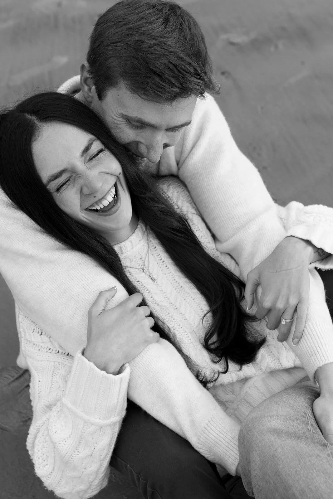 A black and white photo of a couple hugging and laughing together.